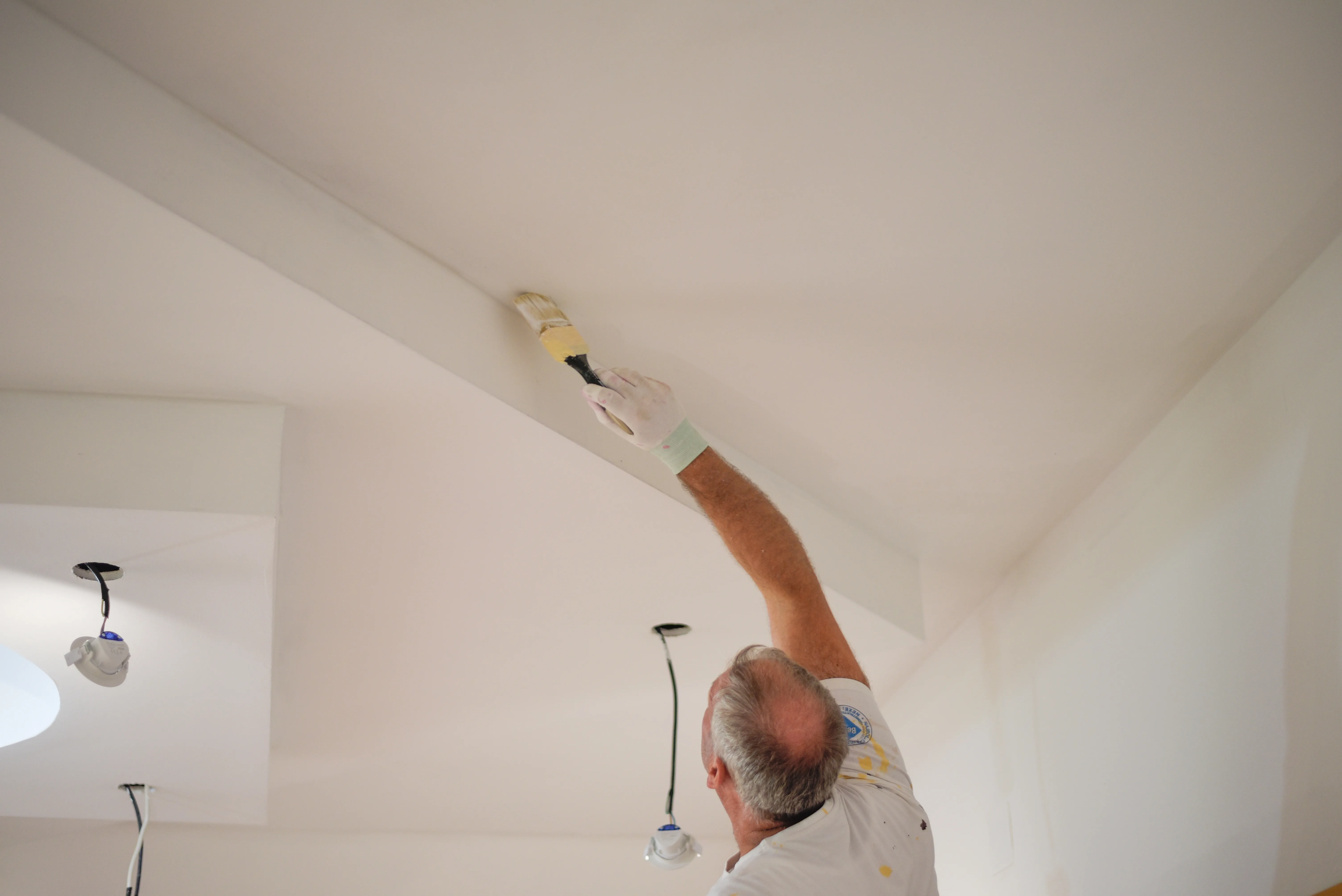 Man painting a ceiling with a brush in a well-lit interior space