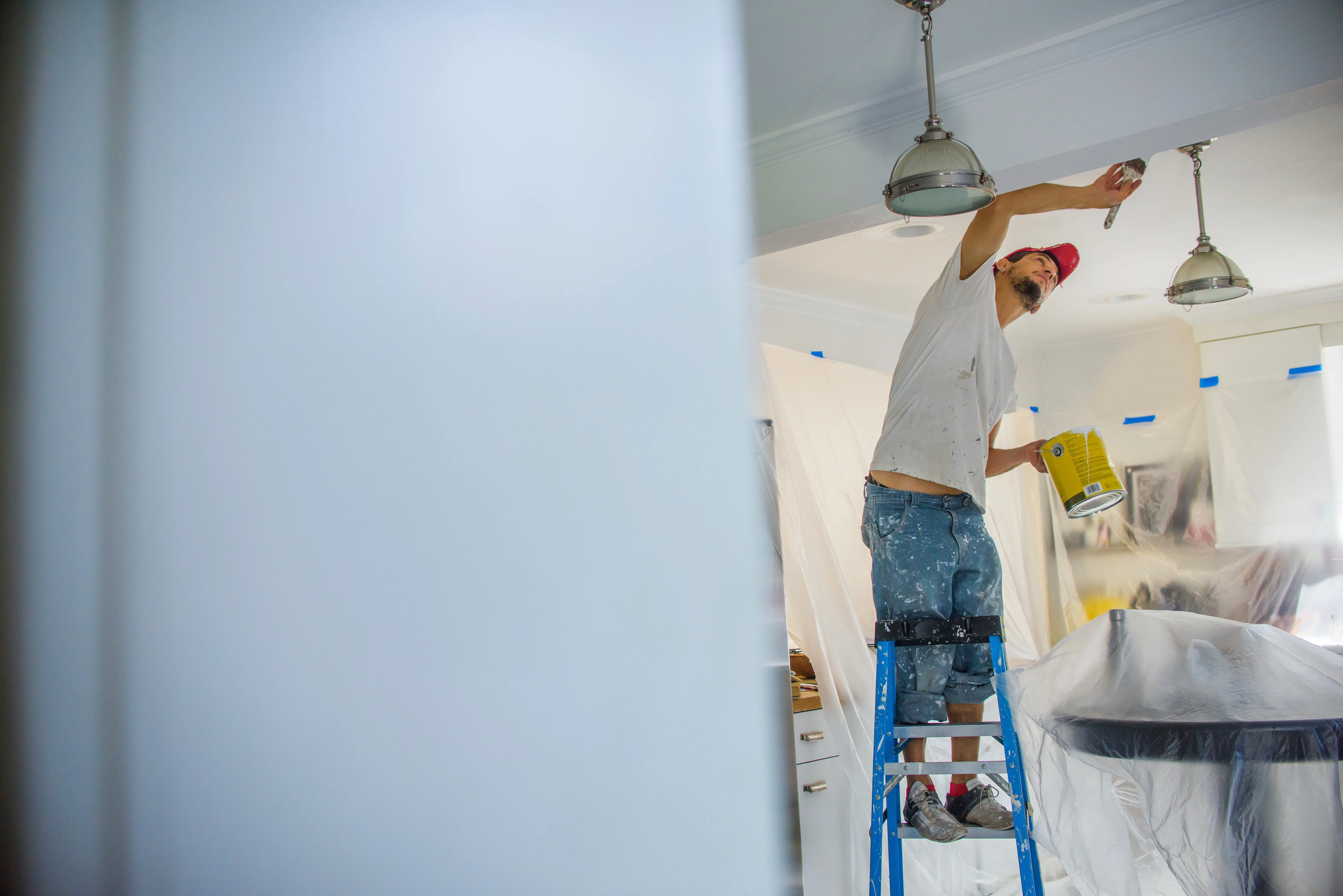 A painter on a ladder applying ceiling paint in a modern kitchen