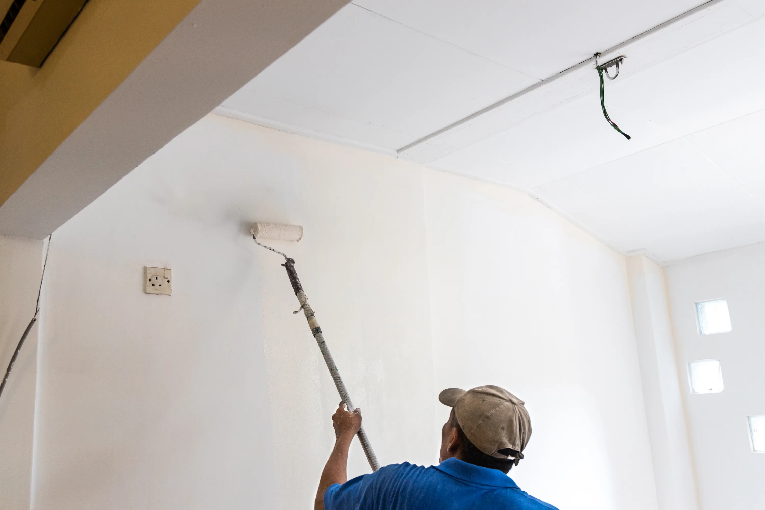 A professional painter using a roller to apply paint on a white ceiling