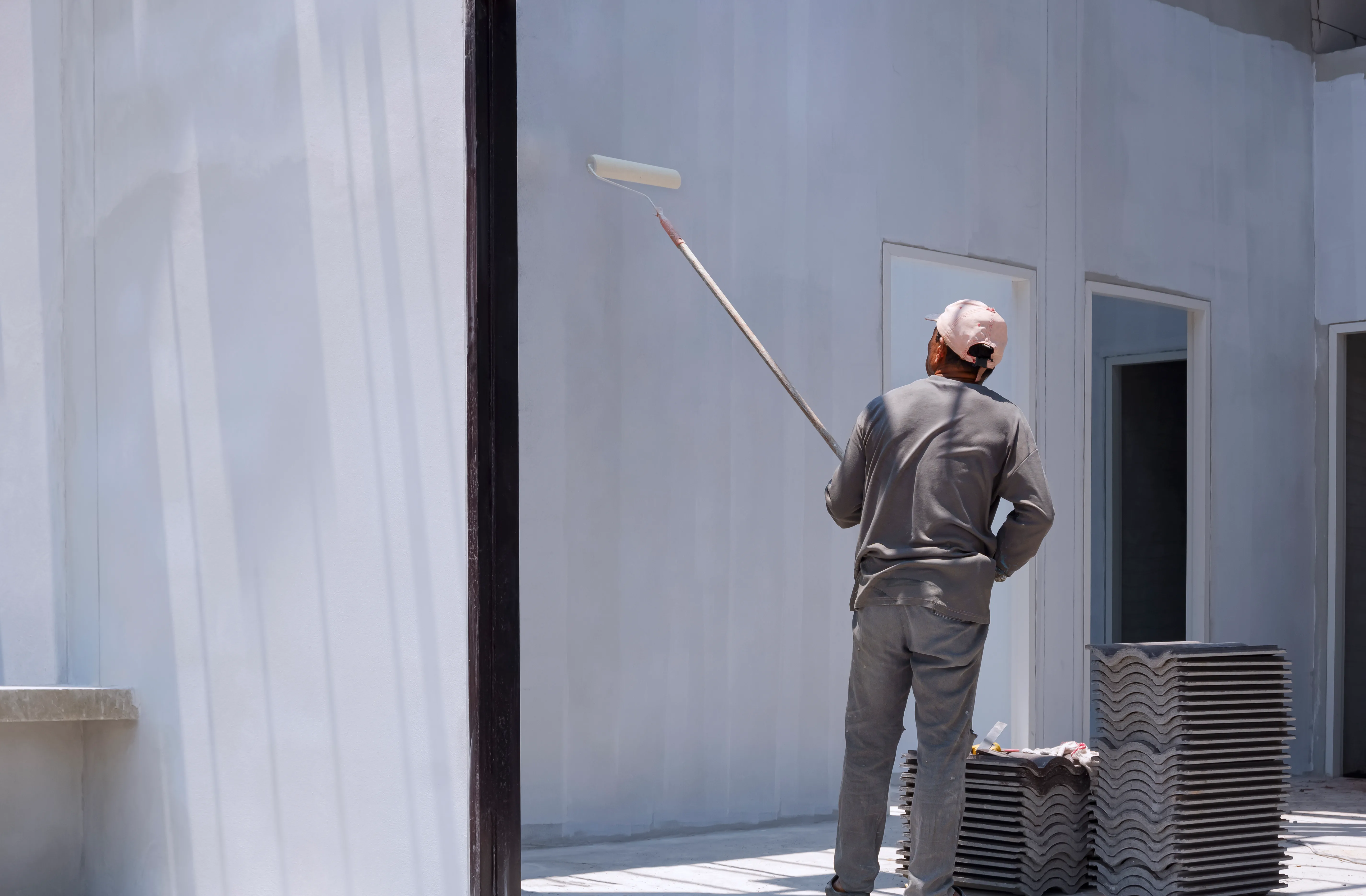 A painter applying a coat of exterior wall paint with a roller on a building