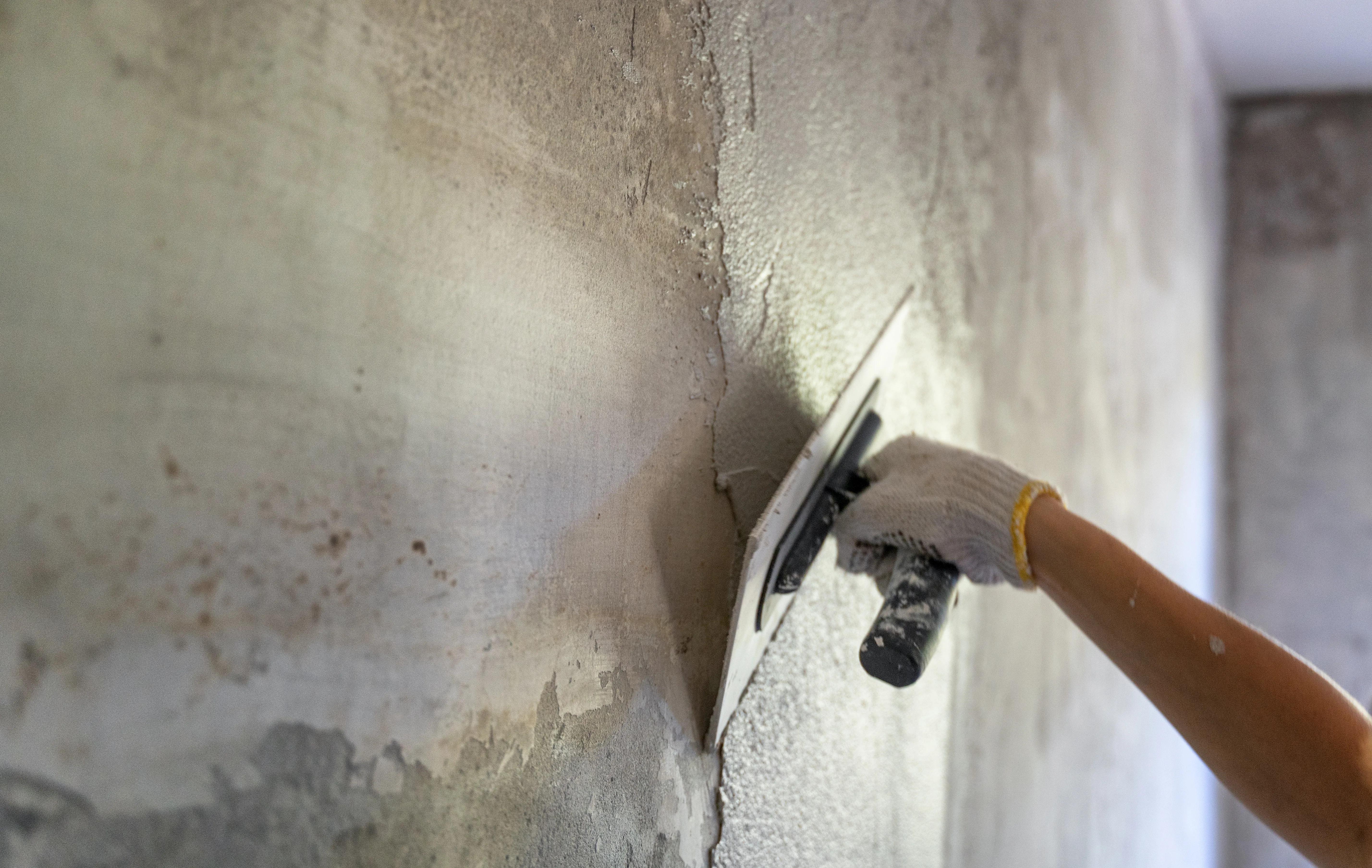 A person applying plaster to a wall using a trowel during surface preparation