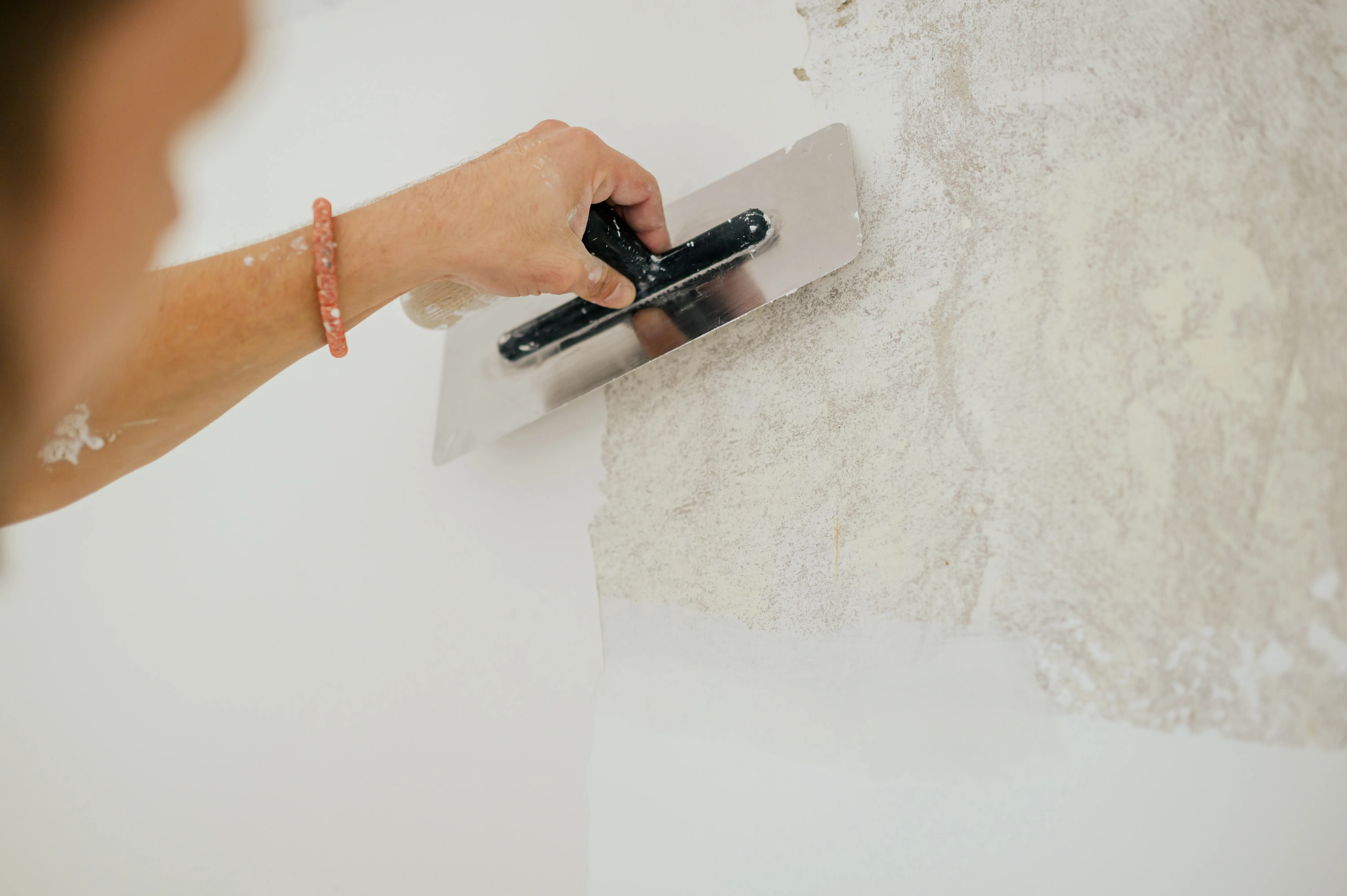 A person applying a smoothing technique to a wall surface with a putty knife