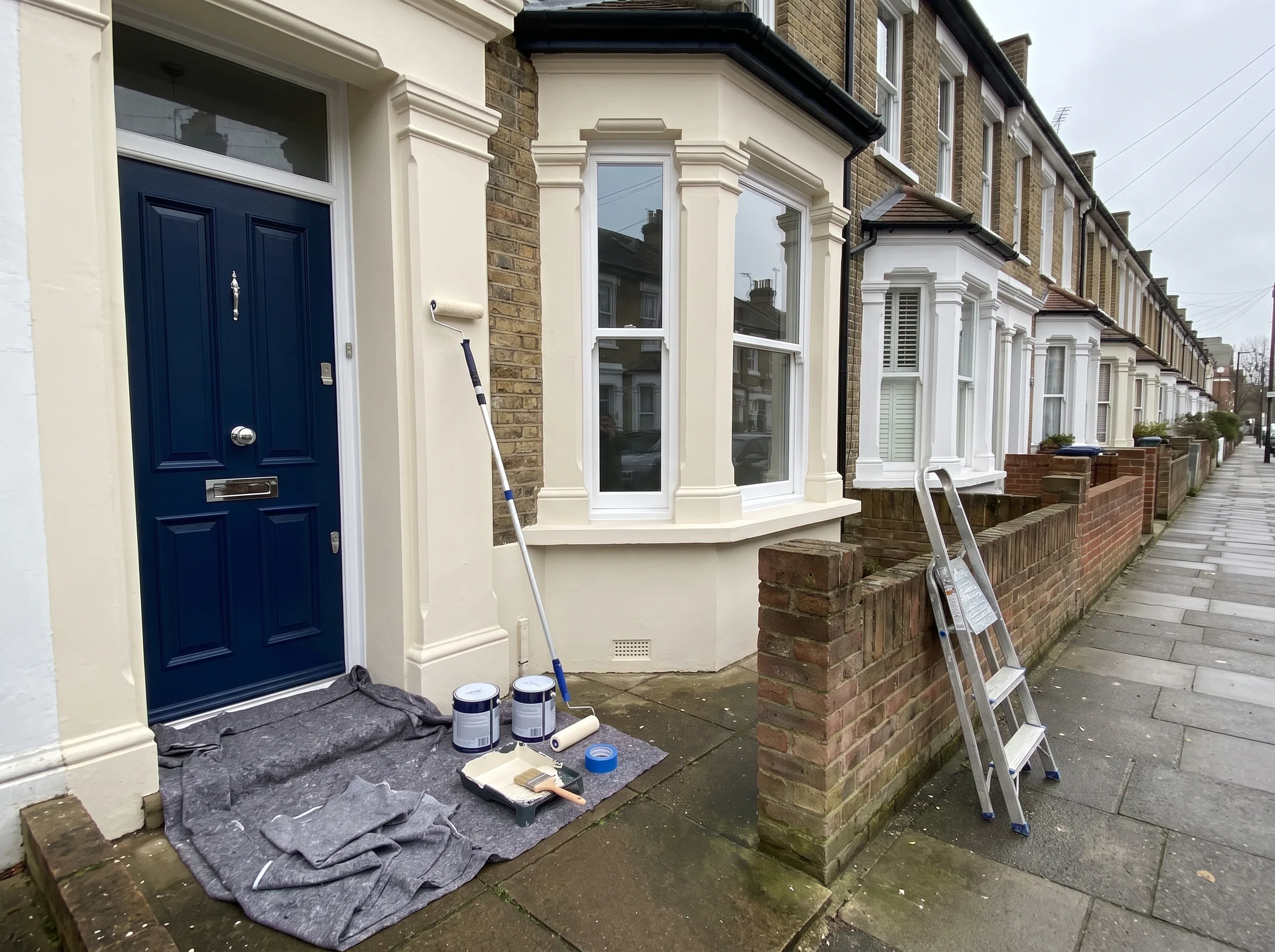 A residential exterior featuring blue door with painting supplies and ladder nearby