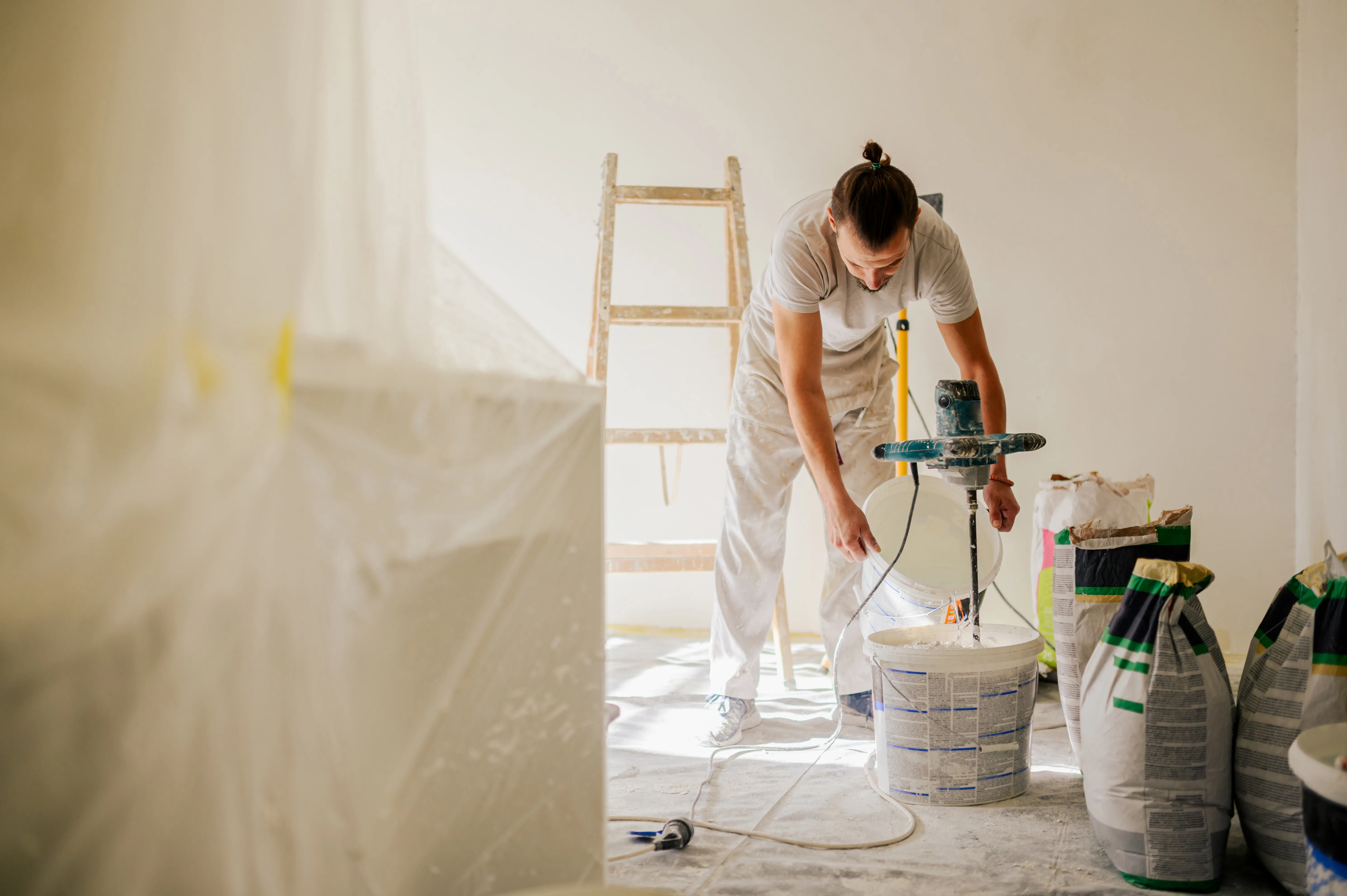 A painter mixes paint in a bucket while preparing for interior wall painting in a bright room