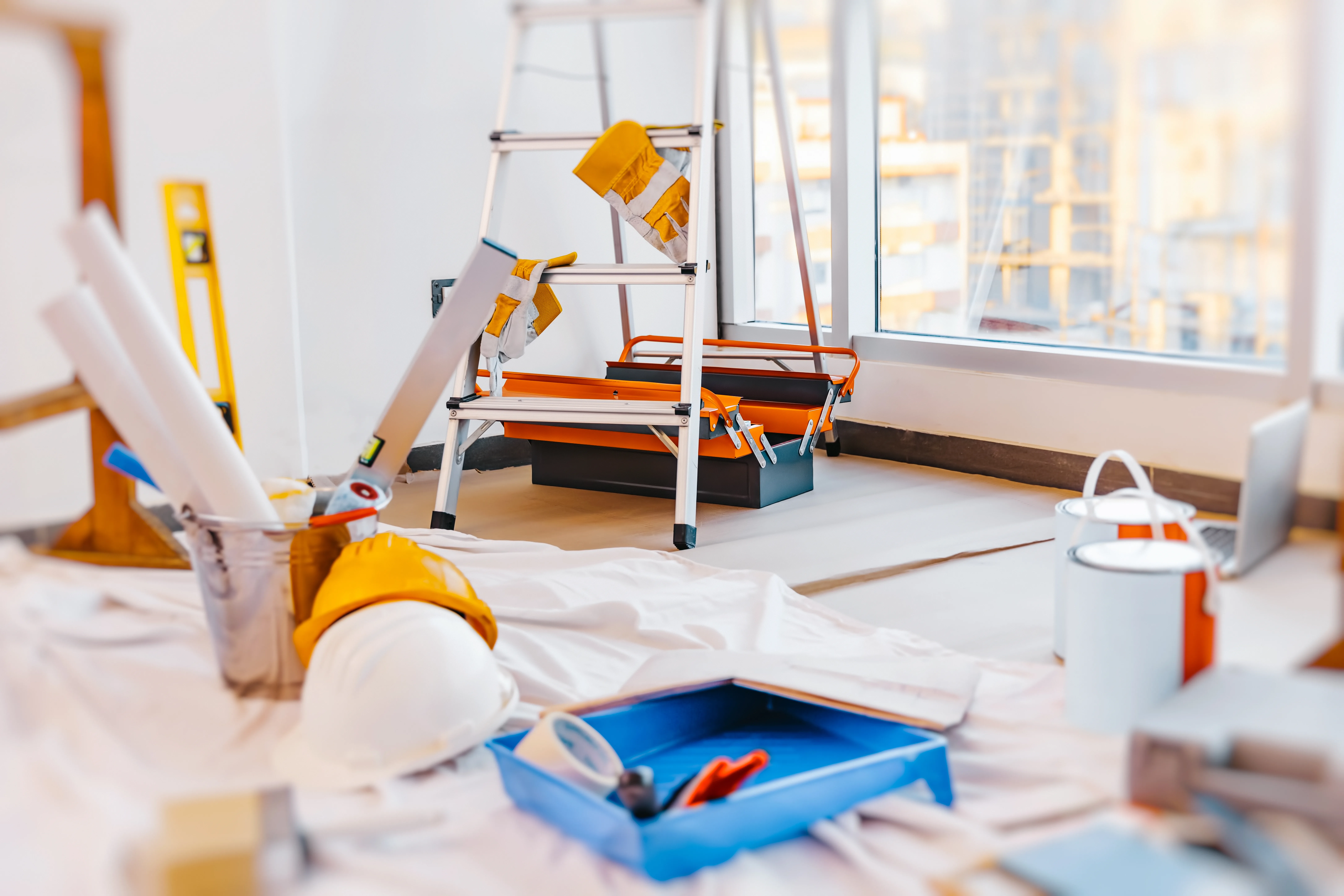 A ladder, painting tools, and materials are organized in a room being prepared for interior decorating
