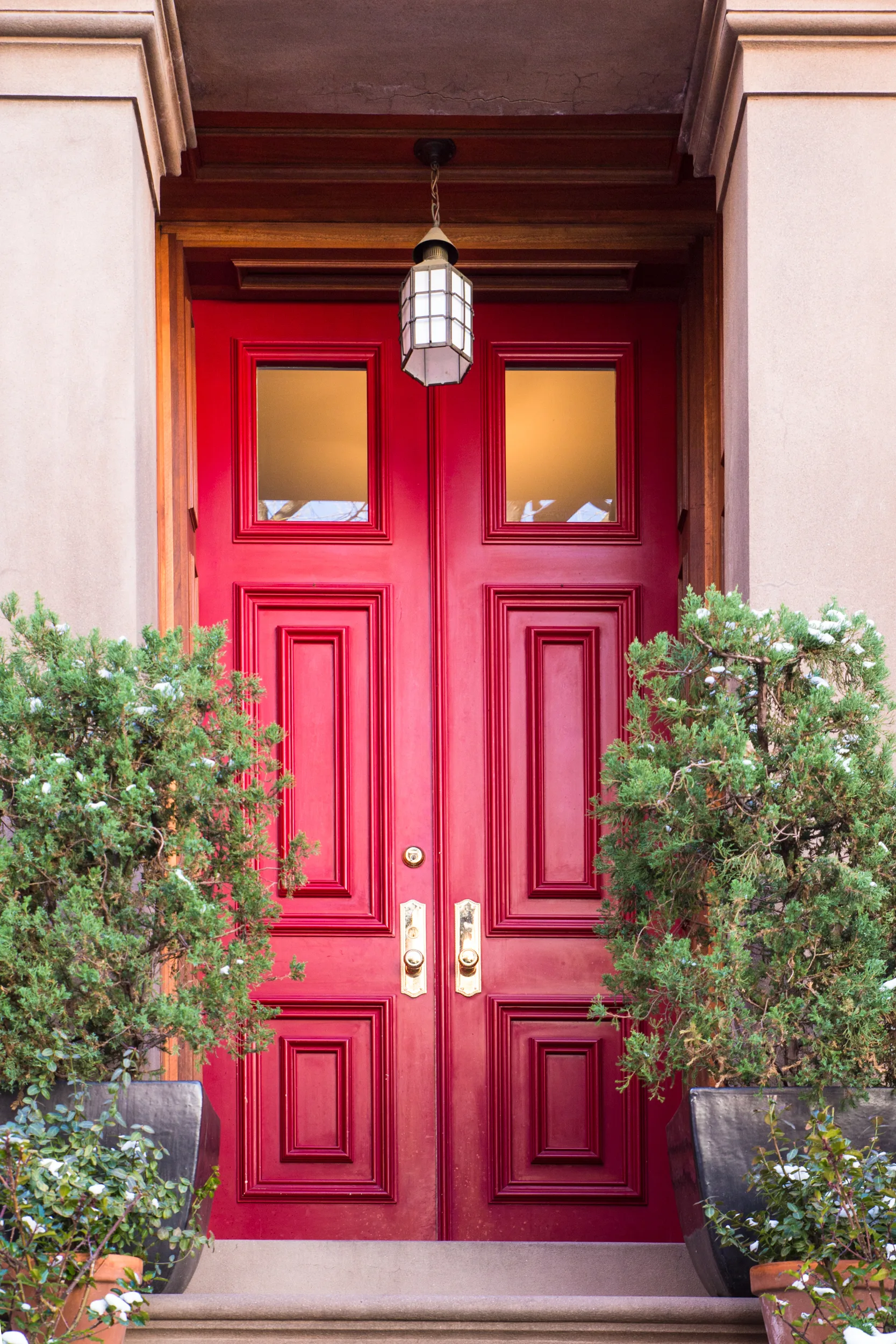Bright red front door with detailed panels, surrounded by greenery in decorative pots