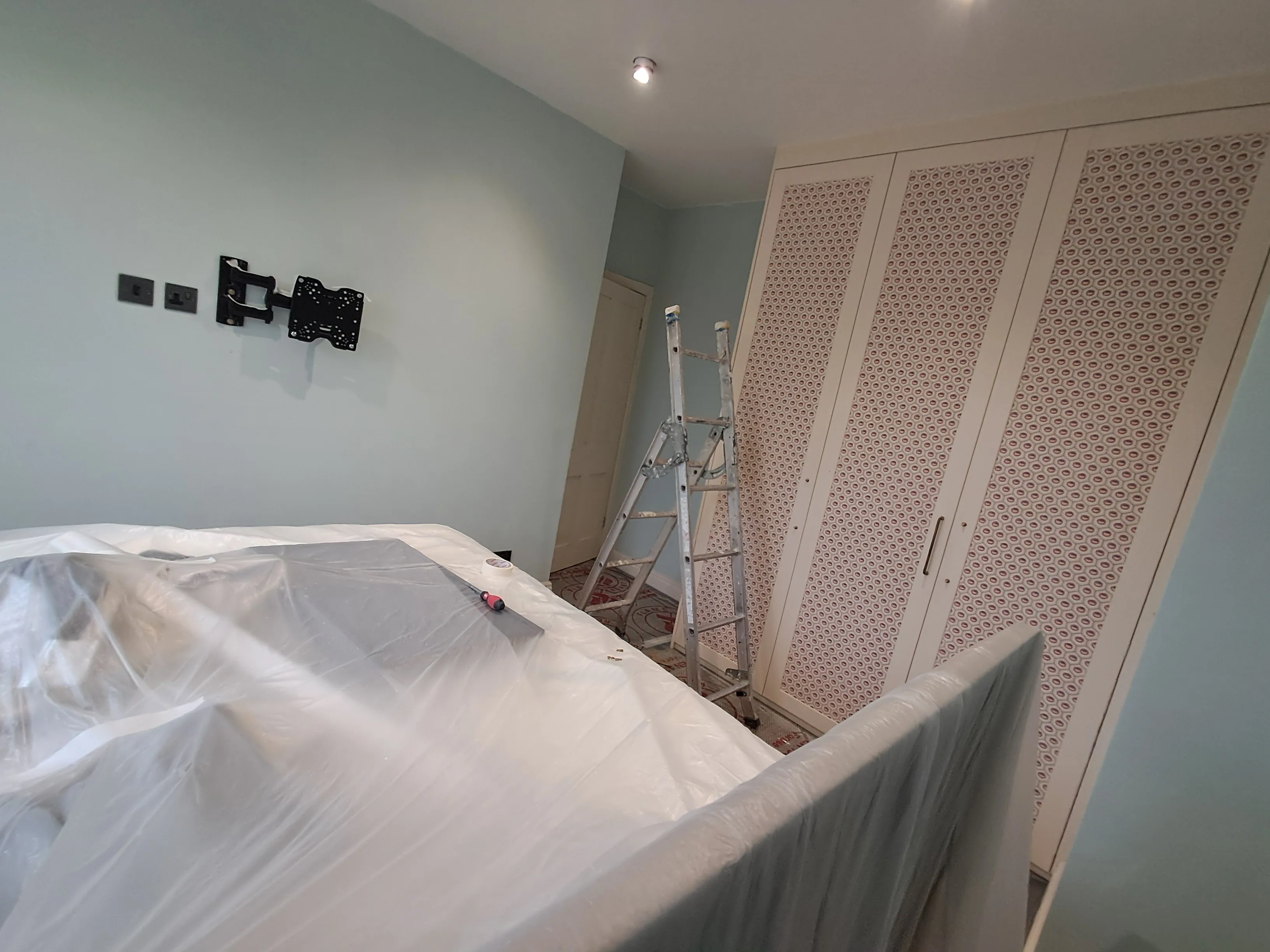 Interior painting preparation with a ladder and covered furniture in a light blue room