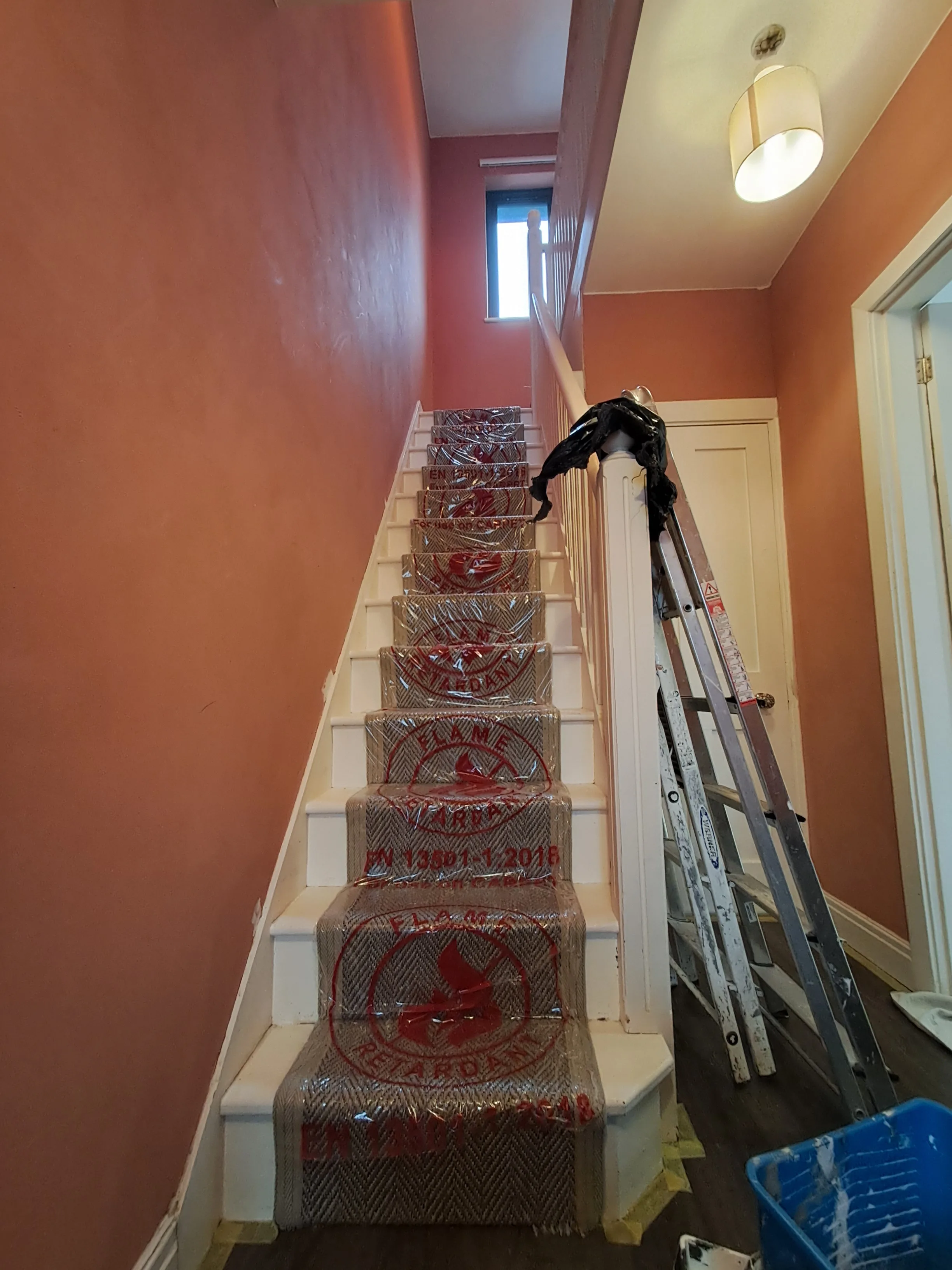 A staircase with protective covering leading to a well-lit landing, featuring freshly painted walls