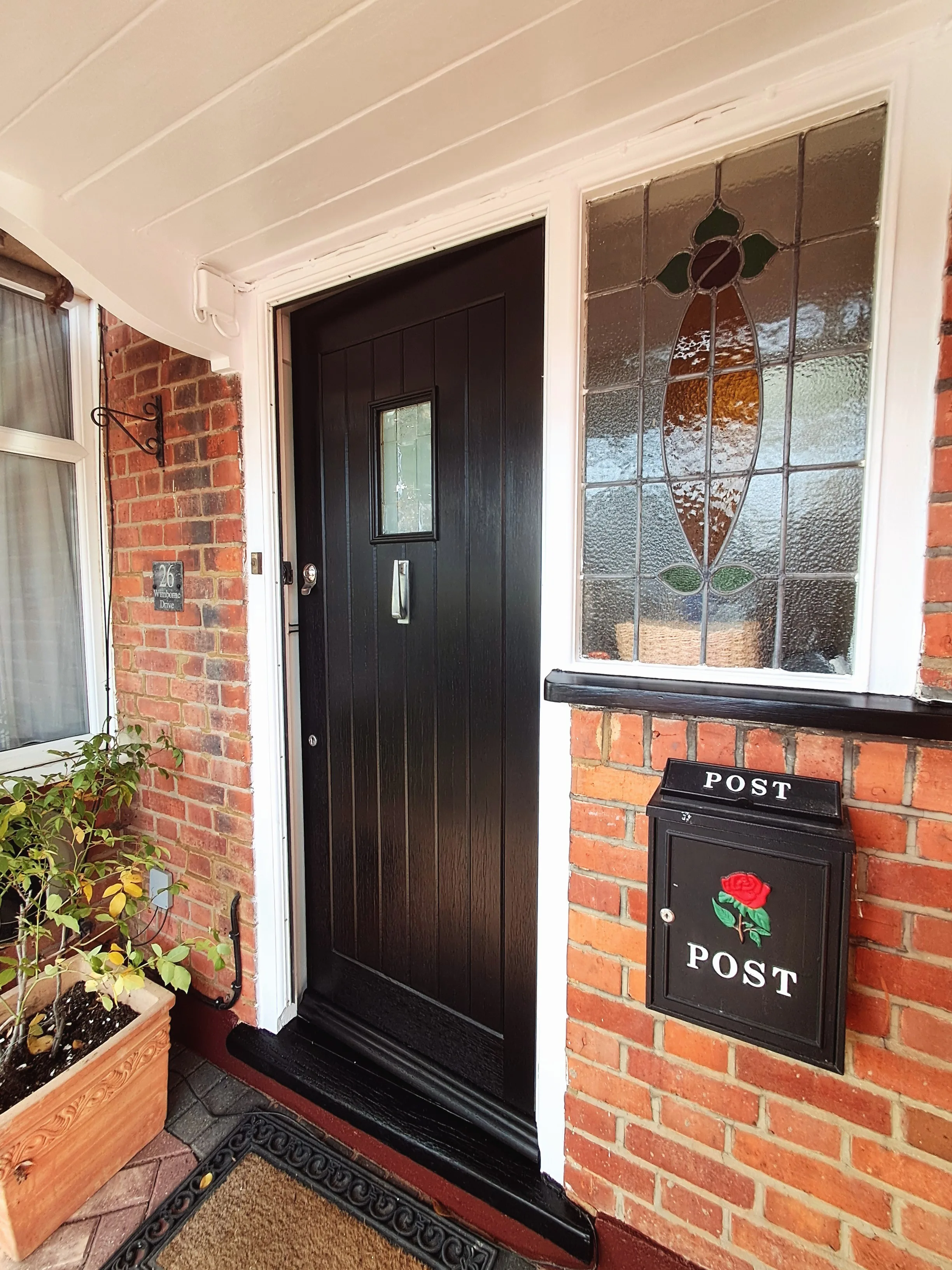 A black front door with decorative glass and a mail slot, next to a brick wall and a mailbox