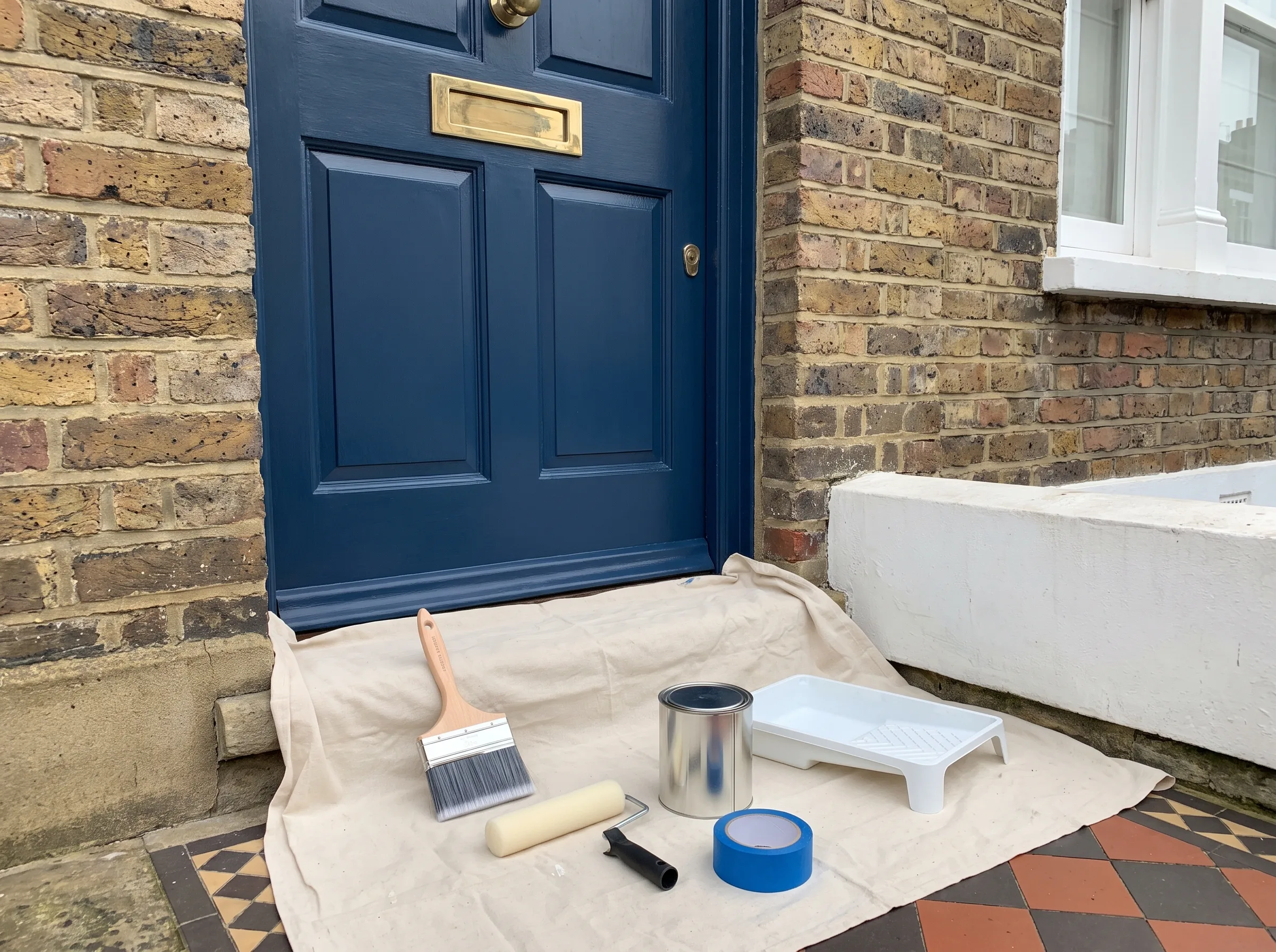 A freshly prepared blue door with painting tools on a drop cloth, ready for door painting