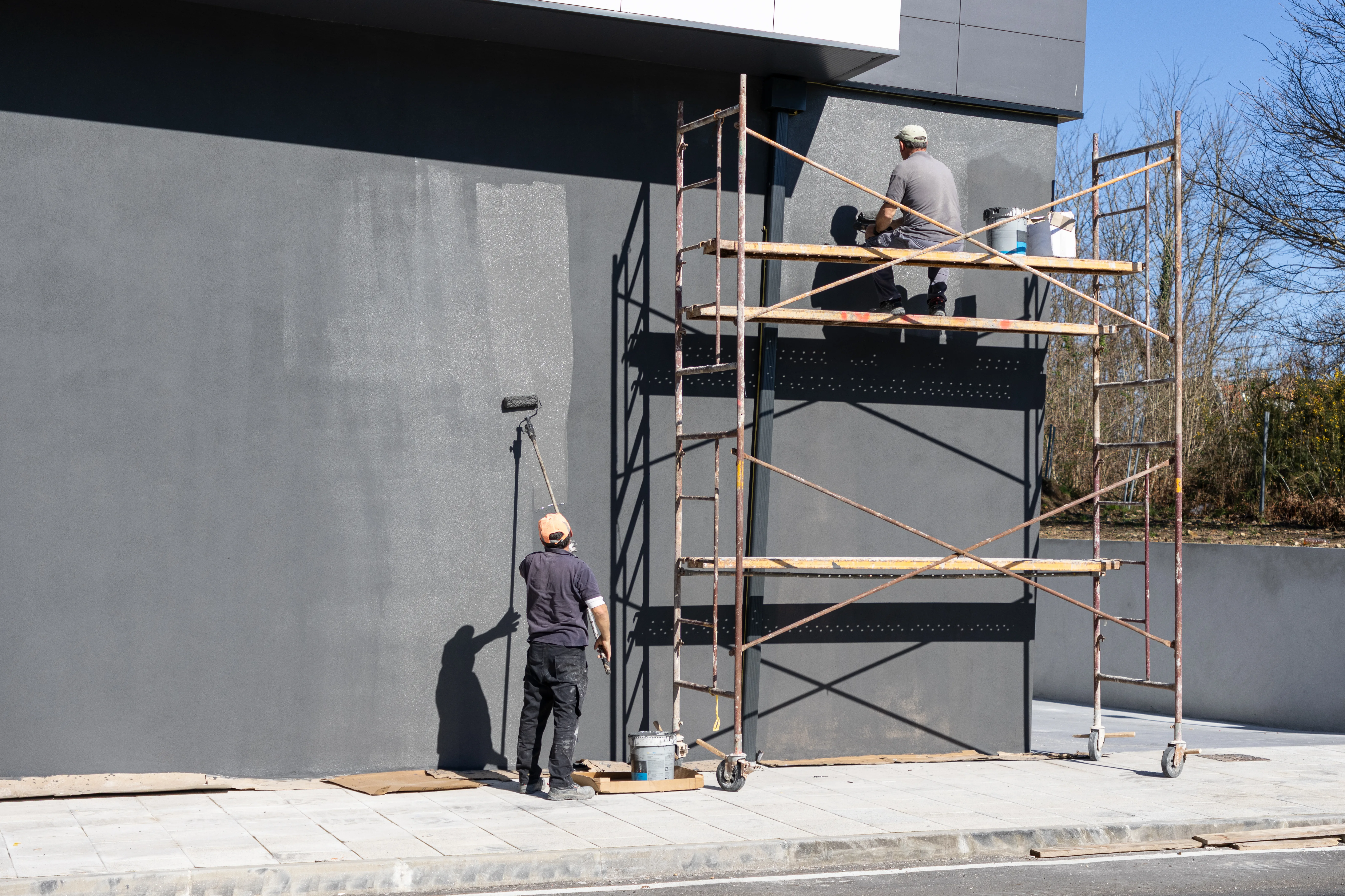 Two painters using scaffolding to apply exterior wall paint on a commercial building
