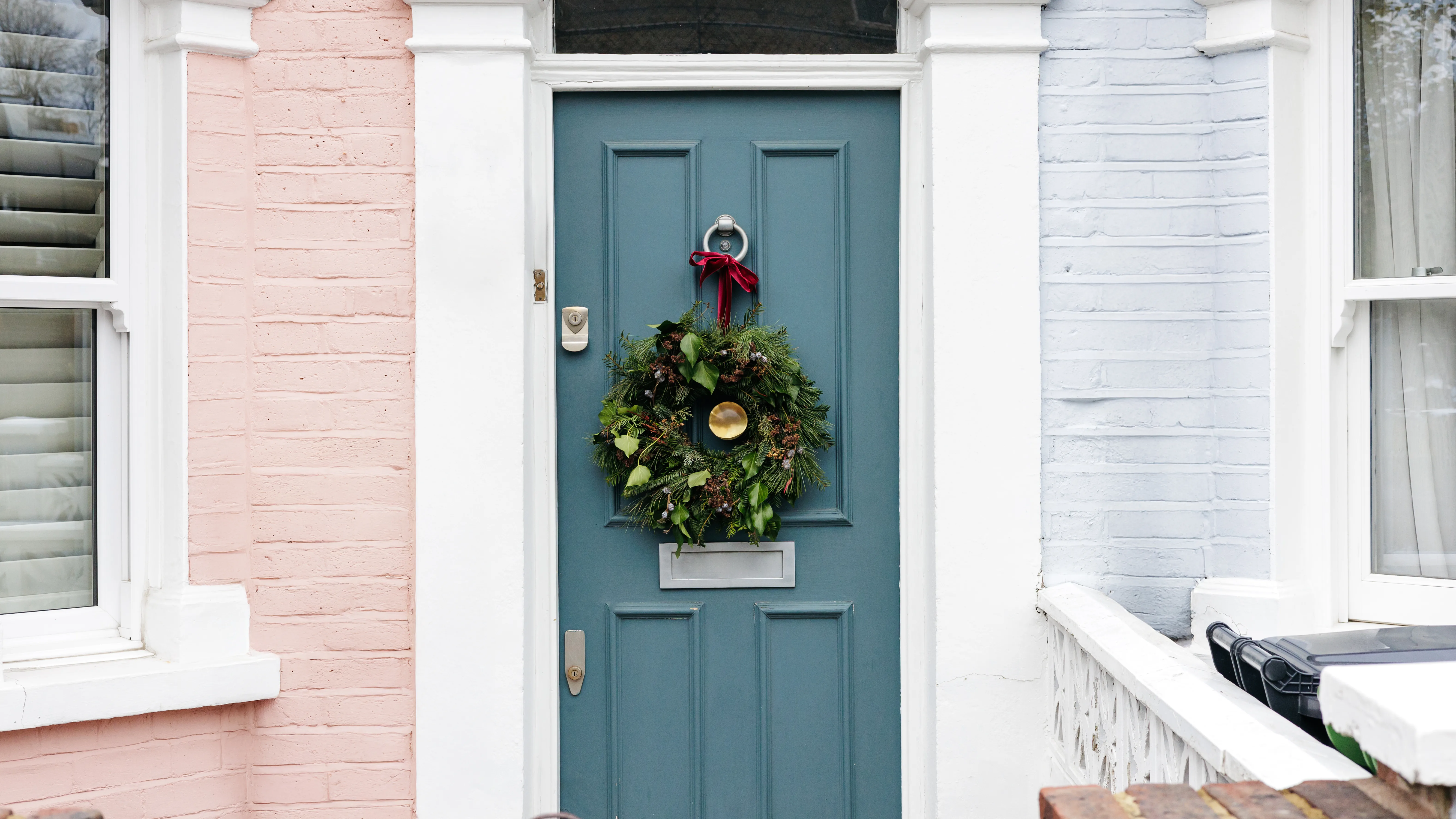 A decorative front door with a wreath, flanked by pastel-colored walls and windows