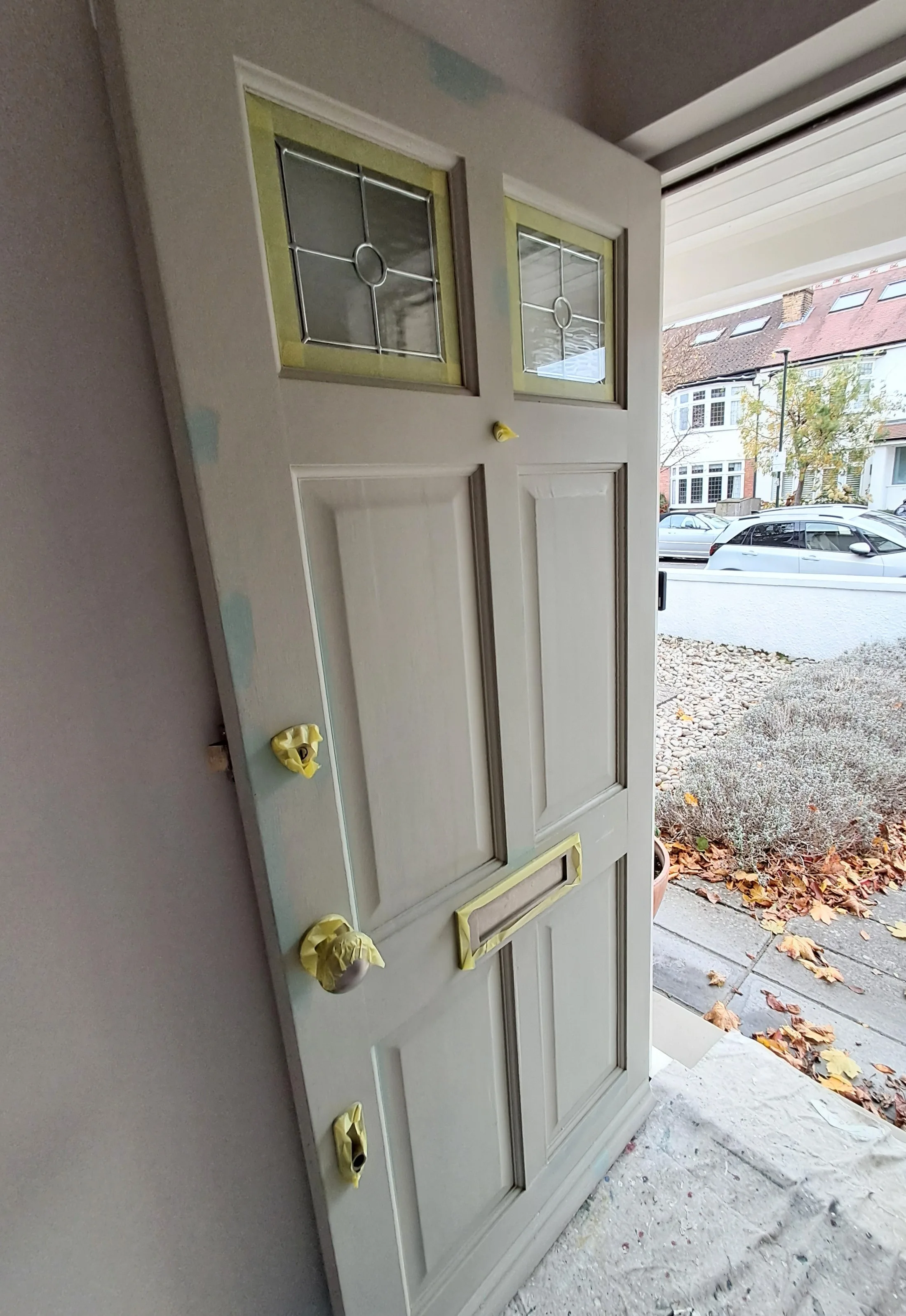 A partially painted front door with glass panels, prepared for final touches outside a home