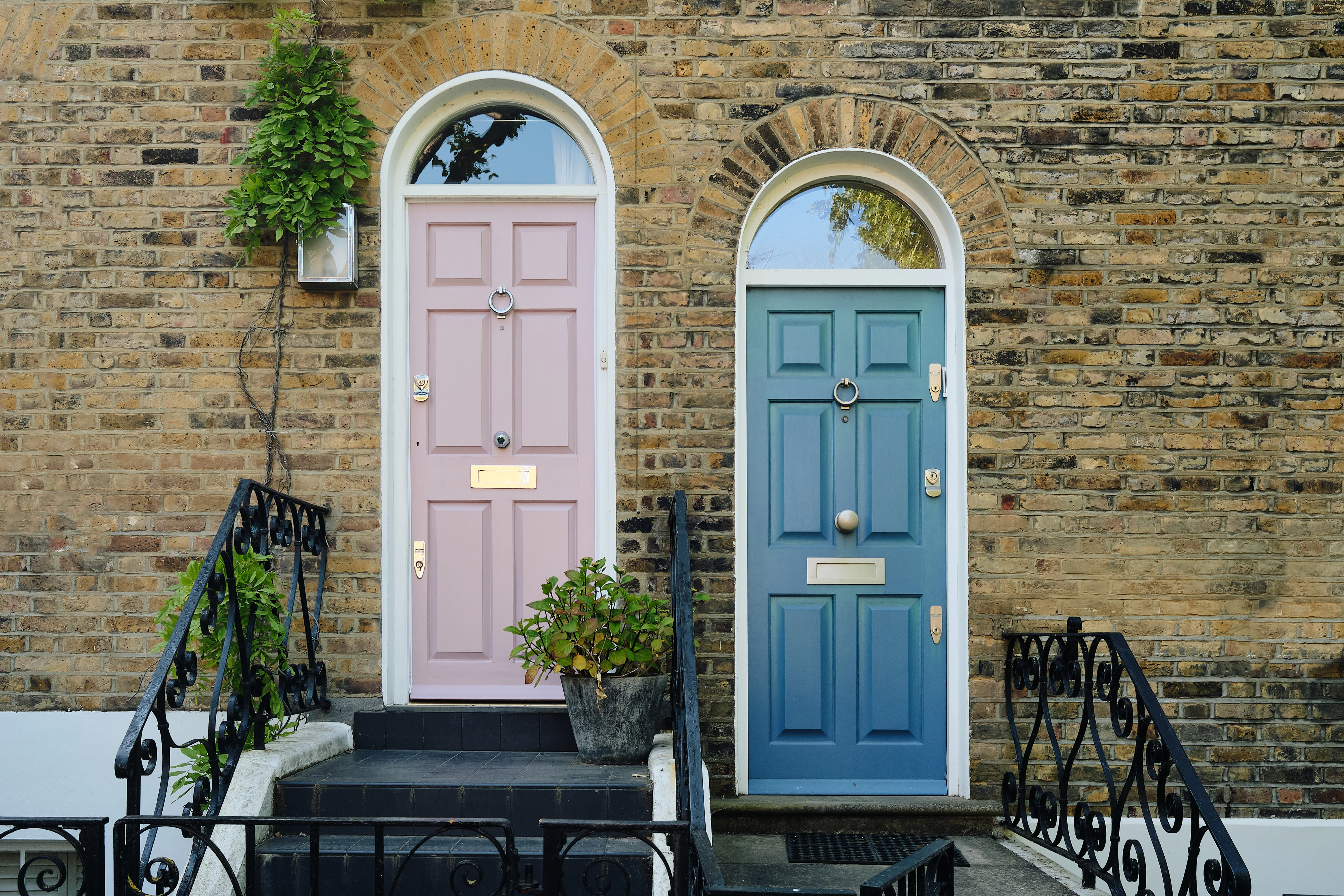 Two colorful front doors framed by a brick wall with decorative plants, showcasing exterior door painting