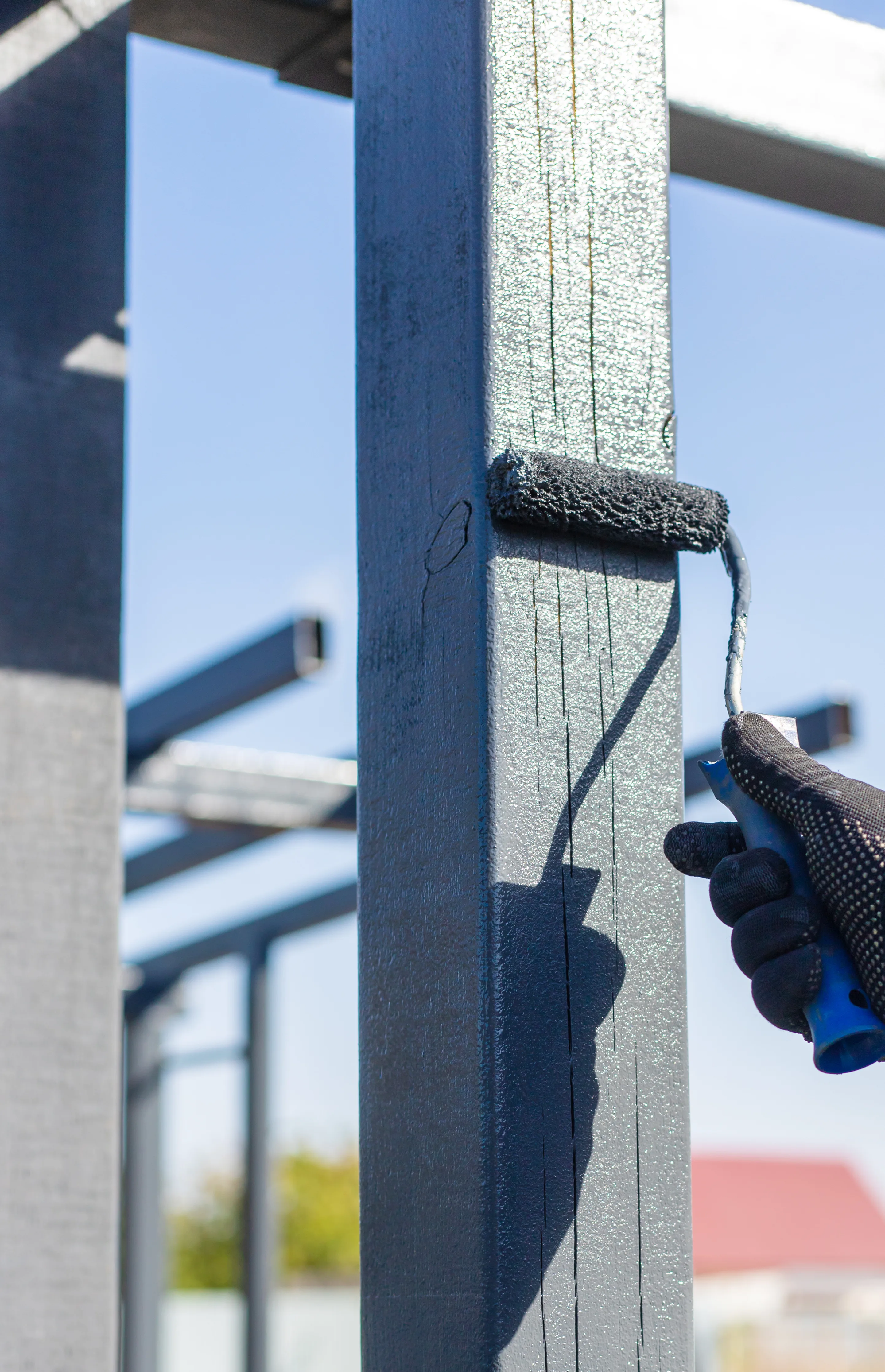 A person painting a wooden post with a roller brush during an exterior painting project