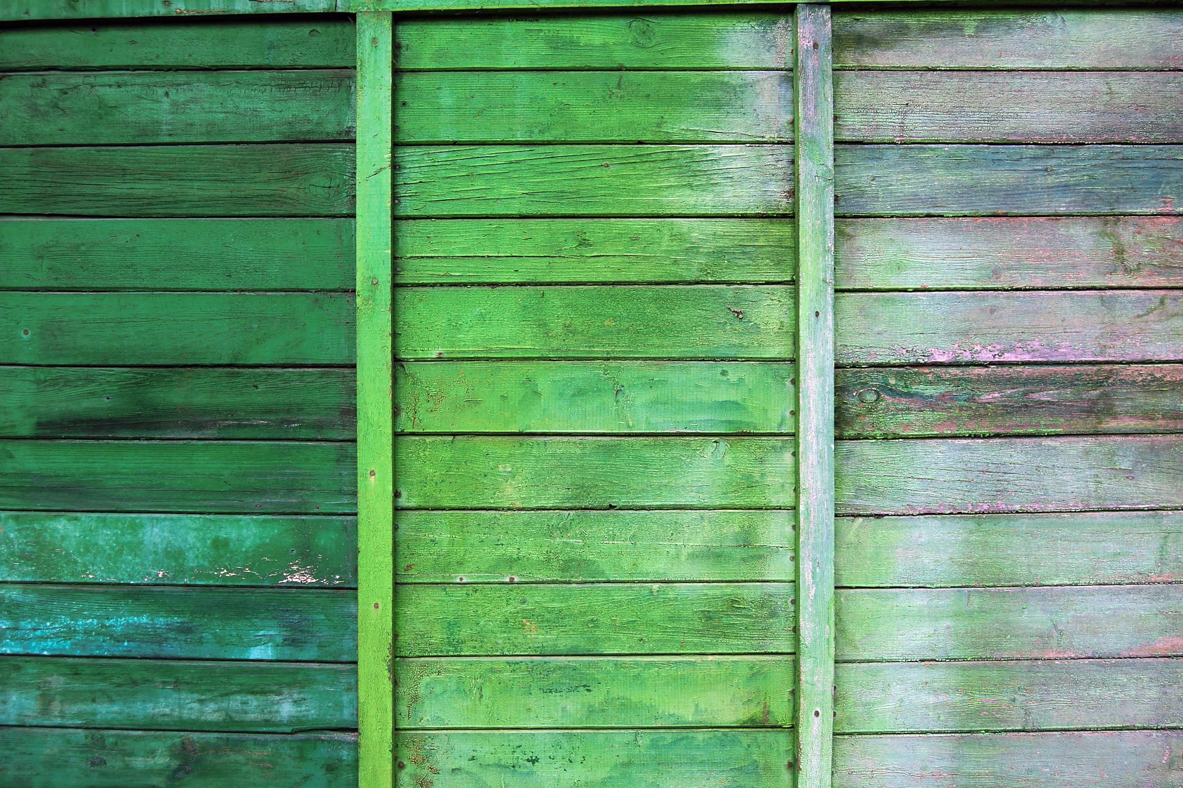Close-up of a wooden fence painted in varying shades of green, showcasing exterior woodwork painting