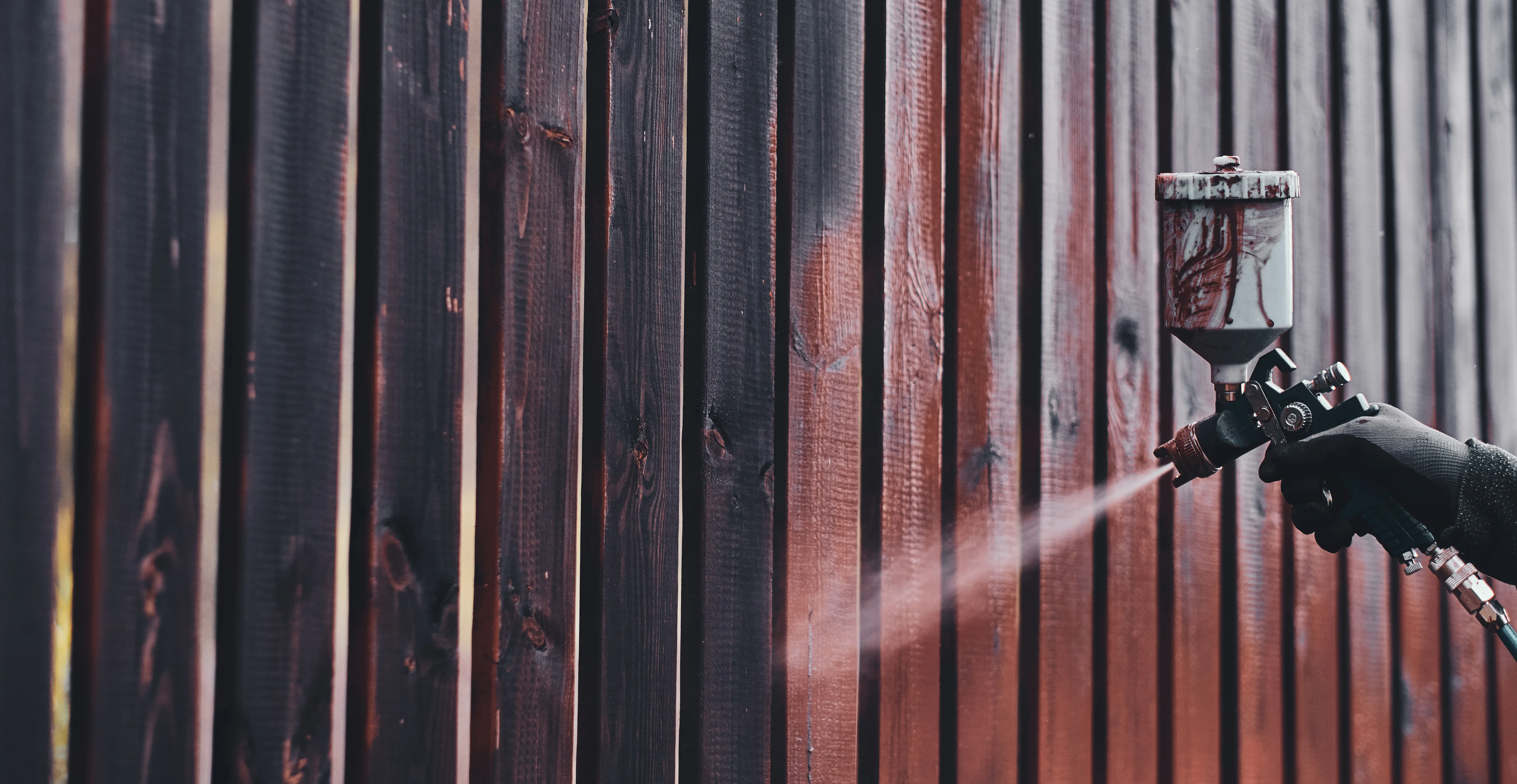 A person spray painting a wooden fence with a spray gun