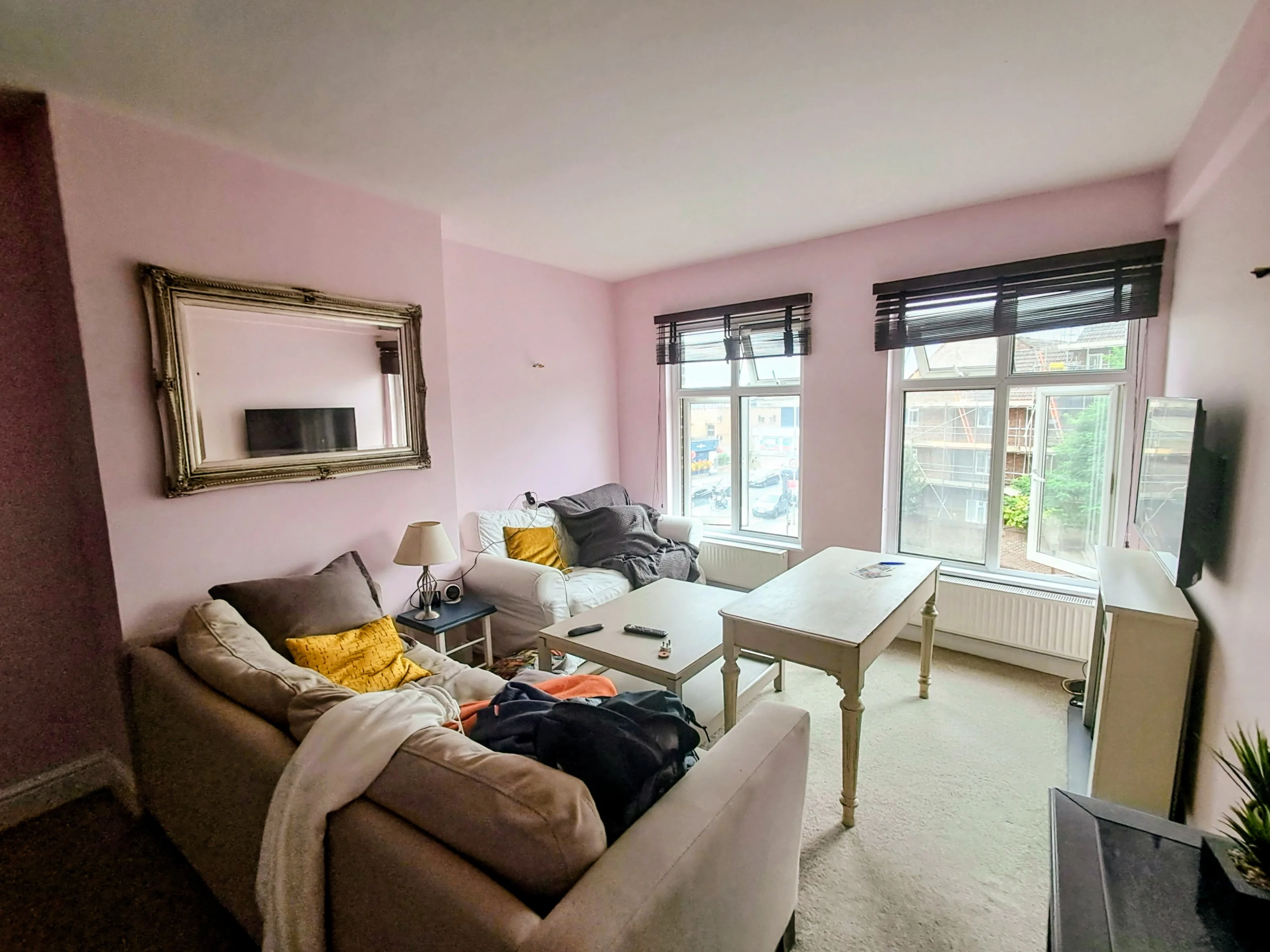 A cozy living room featuring pink walls, comfortable sofas, and a decorative mirror