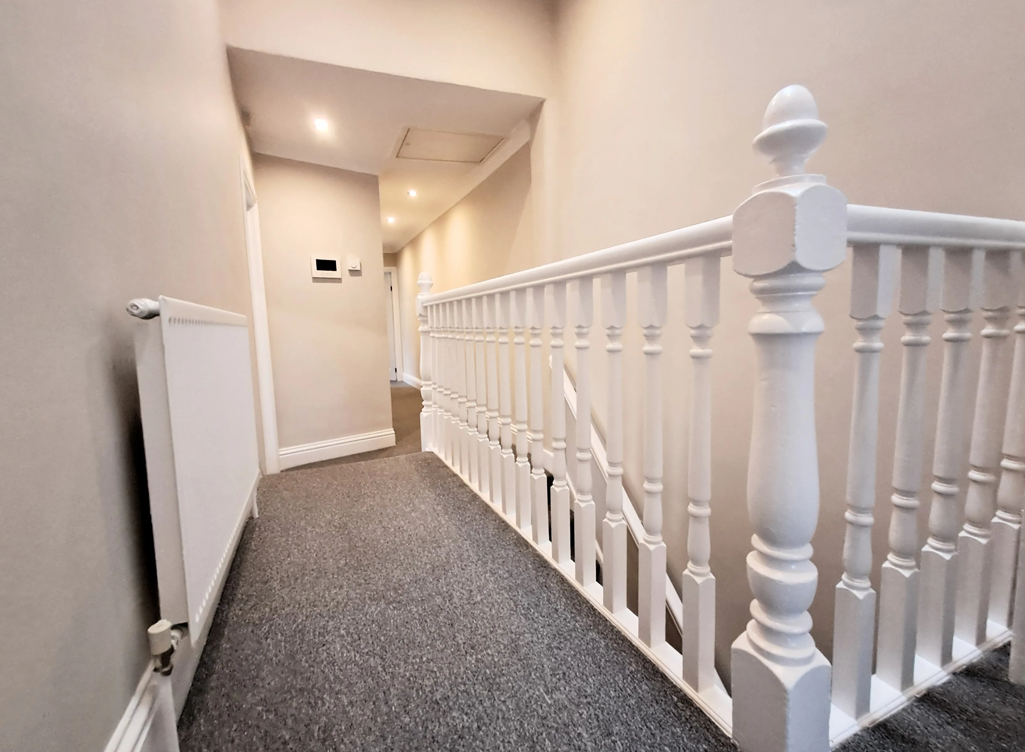 Clean stairway with white wooden railing and gray carpet, showcasing interior painting services