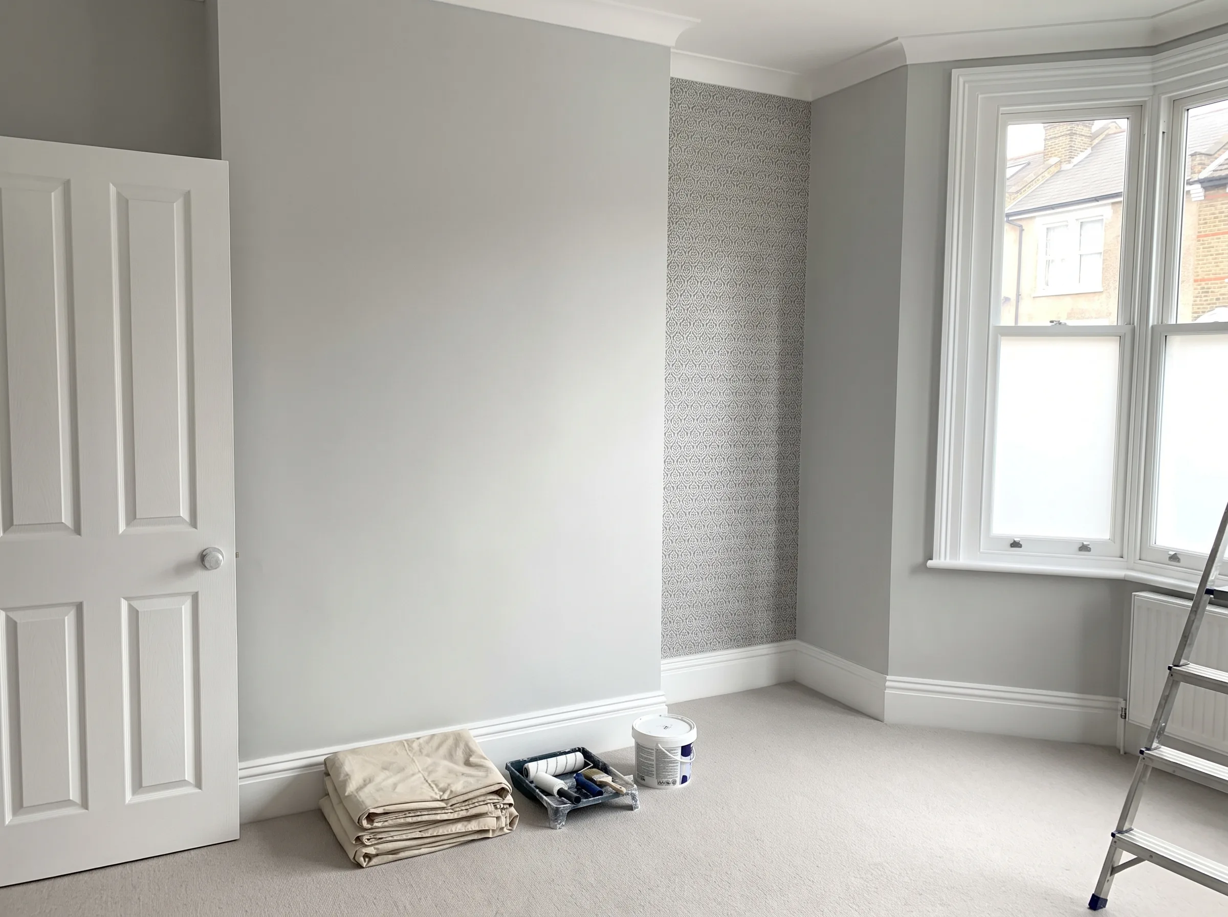 Interior painting setup with a gray wall, paint supplies, and a folded blanket