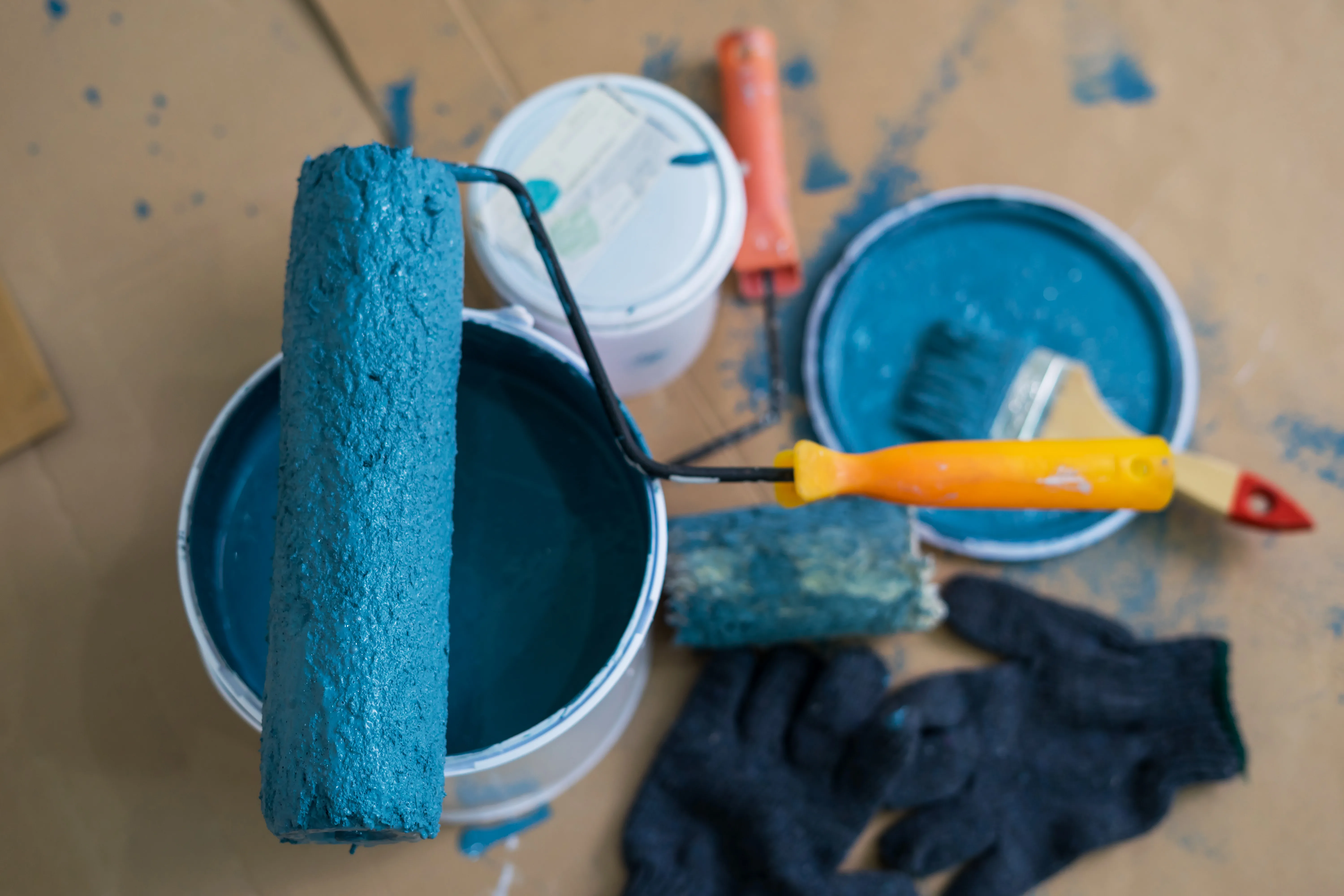 A close-up of a paint roller and containers with teal paint, ready for wall painting