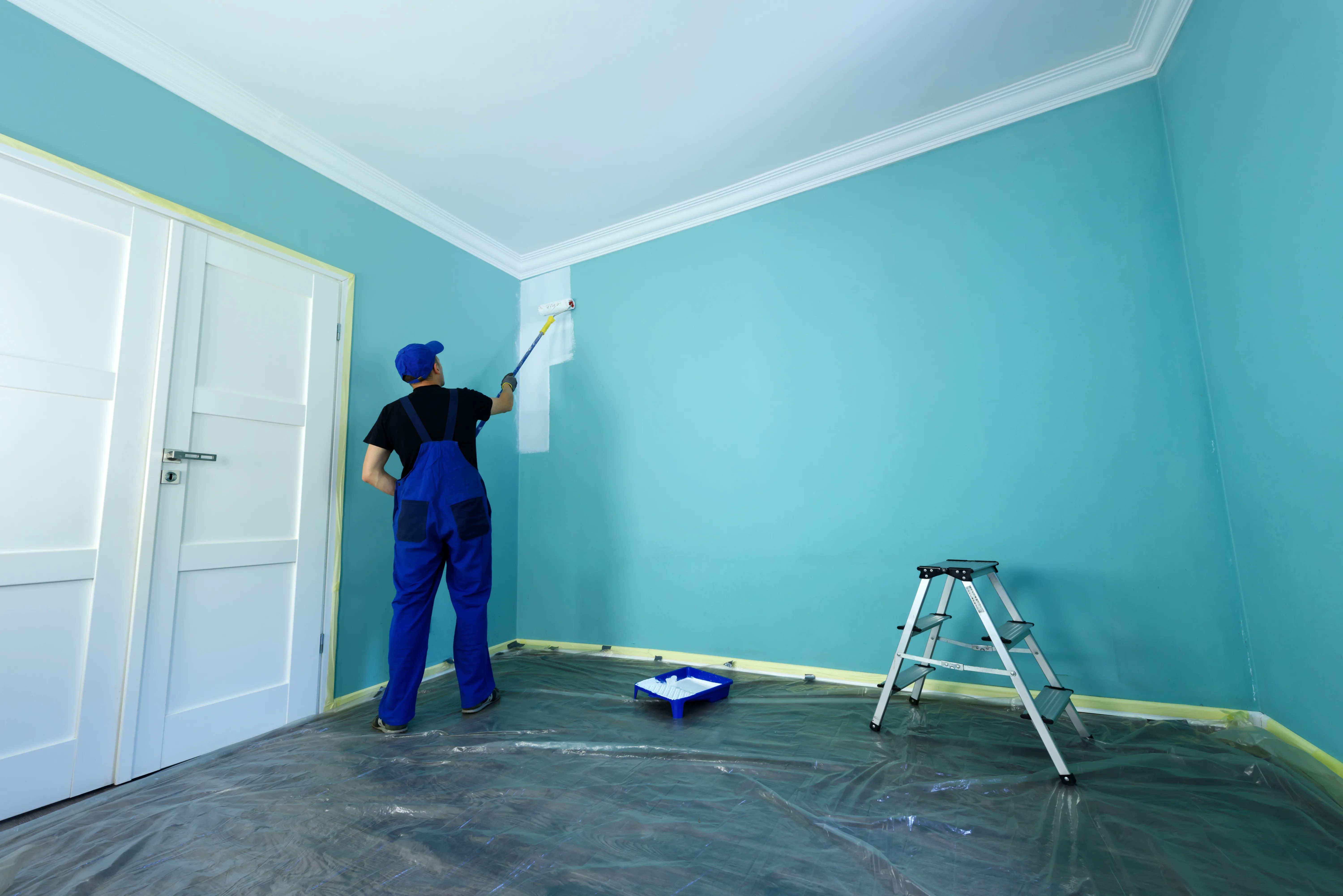 A painter applying a fresh coat of turquoise paint to a wall using a roller