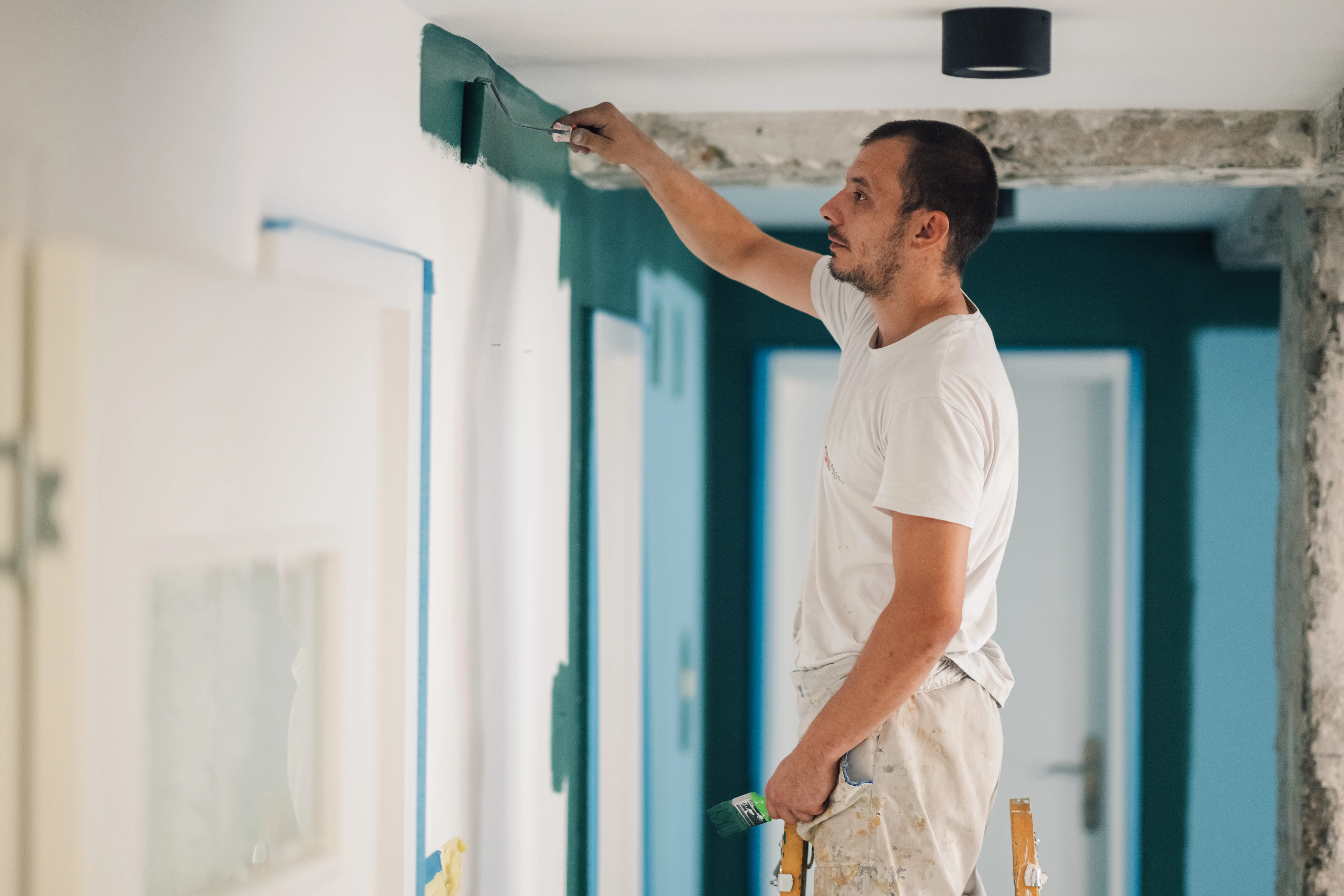 A painter applying a fresh coat of green paint to a wall in a modern interior corridor