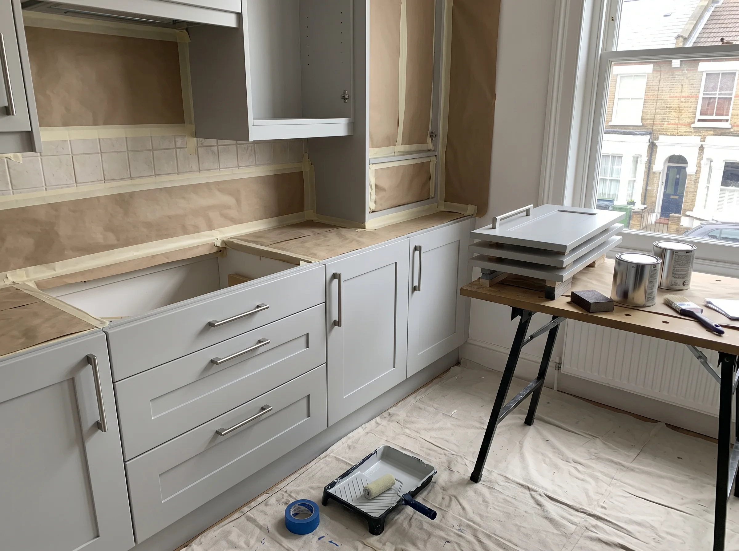 Kitchen cabinet painting in progress with protective coverings and tools visible