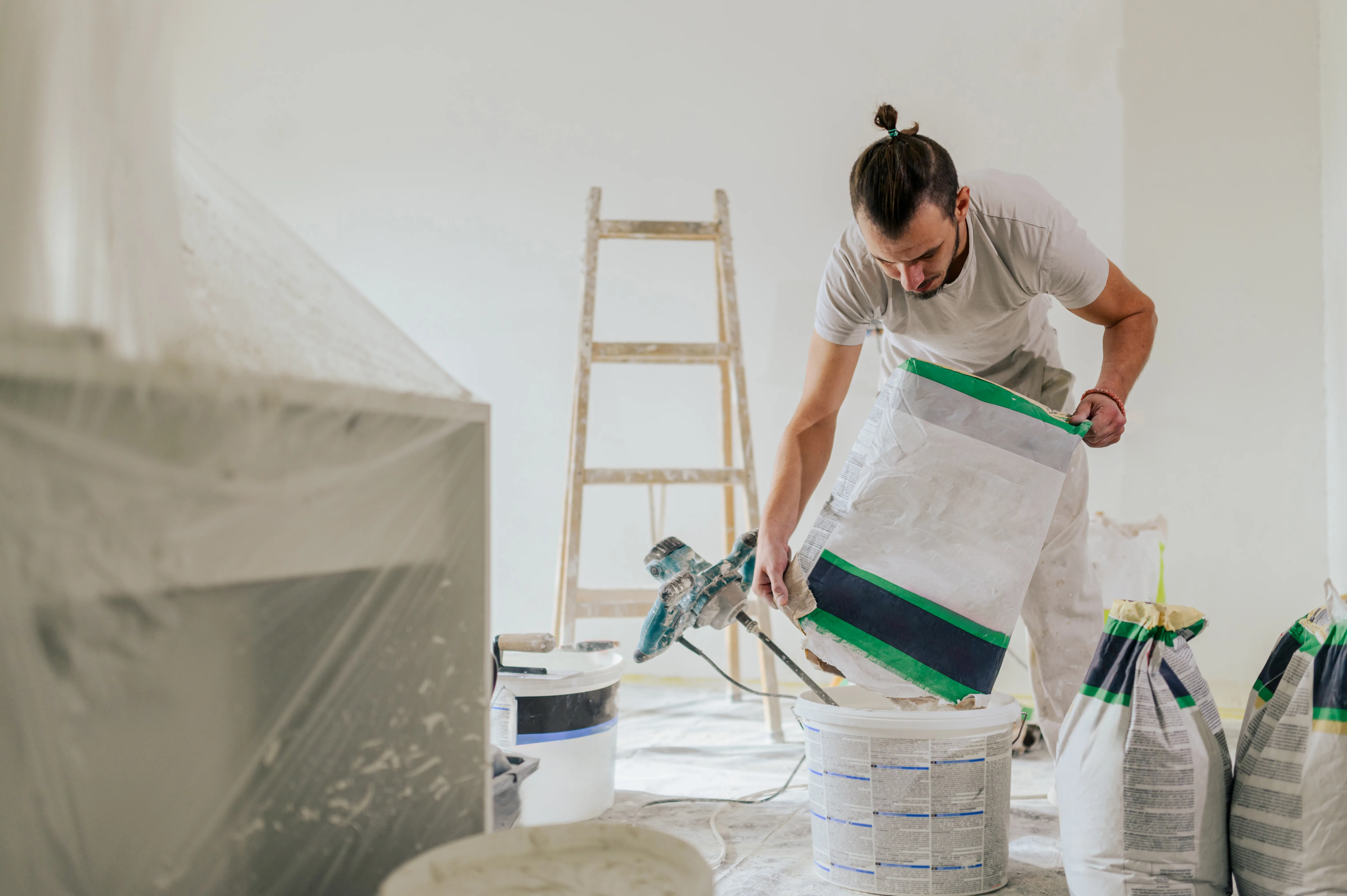A painter preparing paint for interior wall painting with a ladder in the background