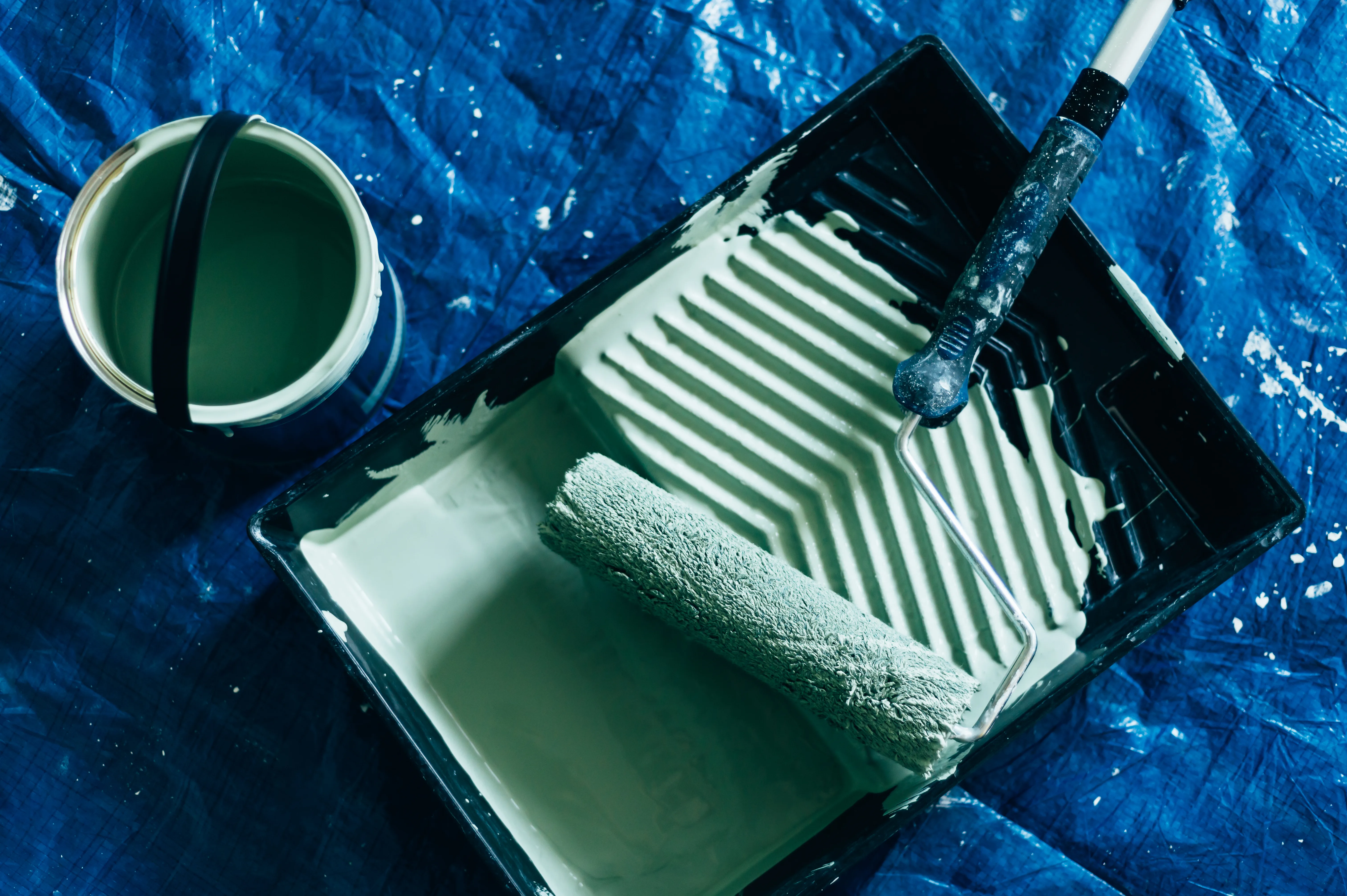 A paint roller and tray filled with green paint on a blue drop cloth