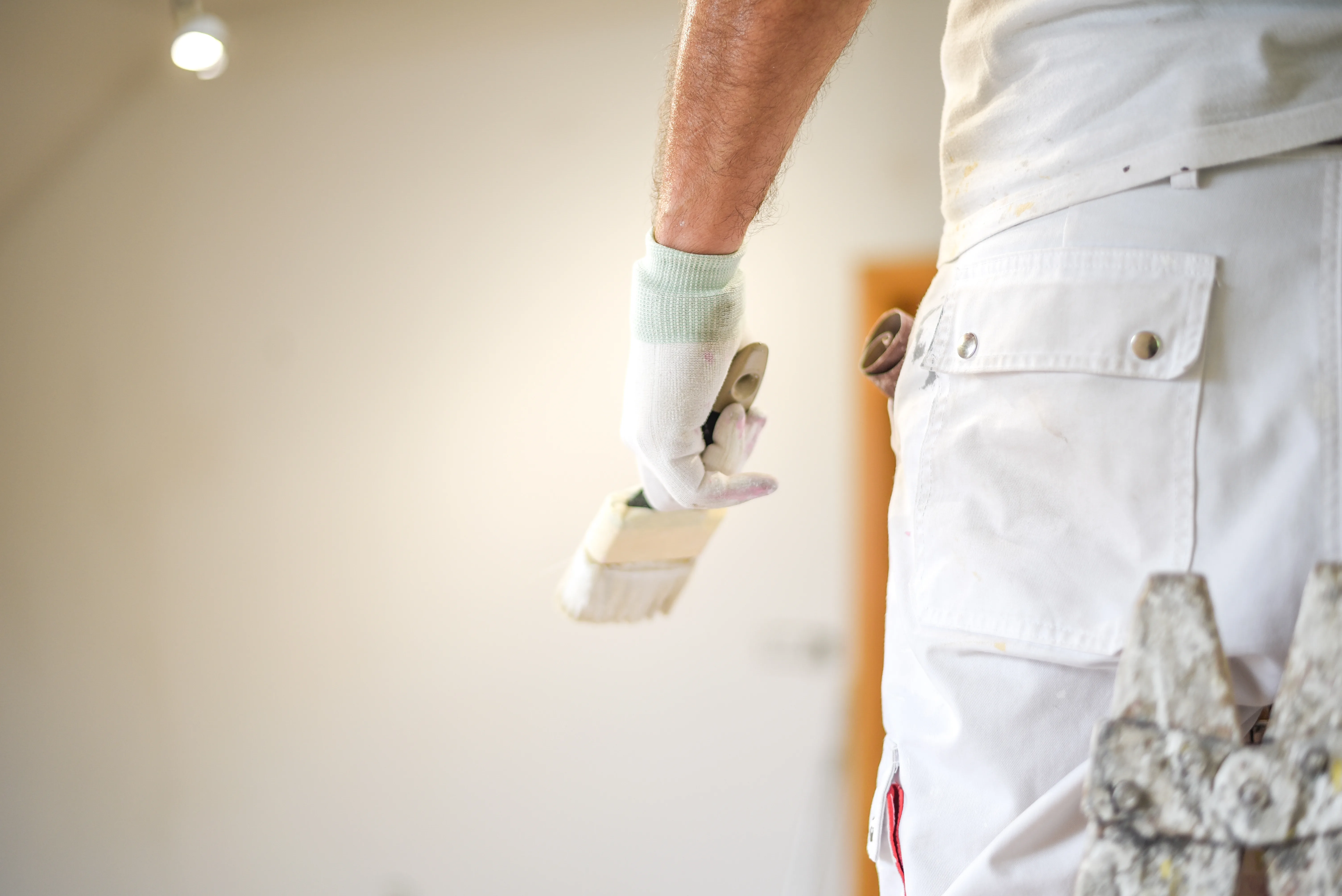 A painter holding a trowel, preparing for interior wall painting in a well-lit room