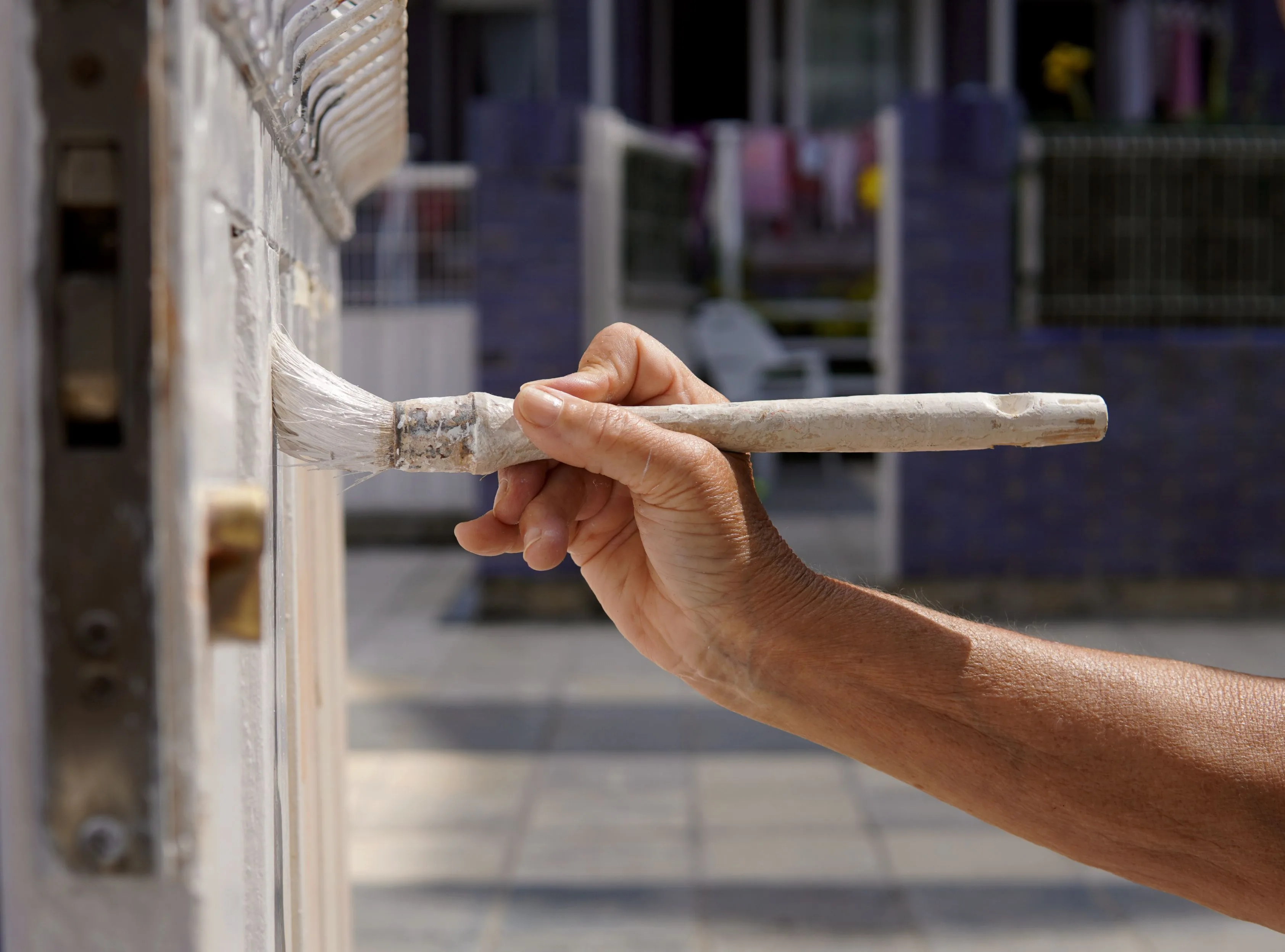 A hand using a paintbrush to apply white paint on a door