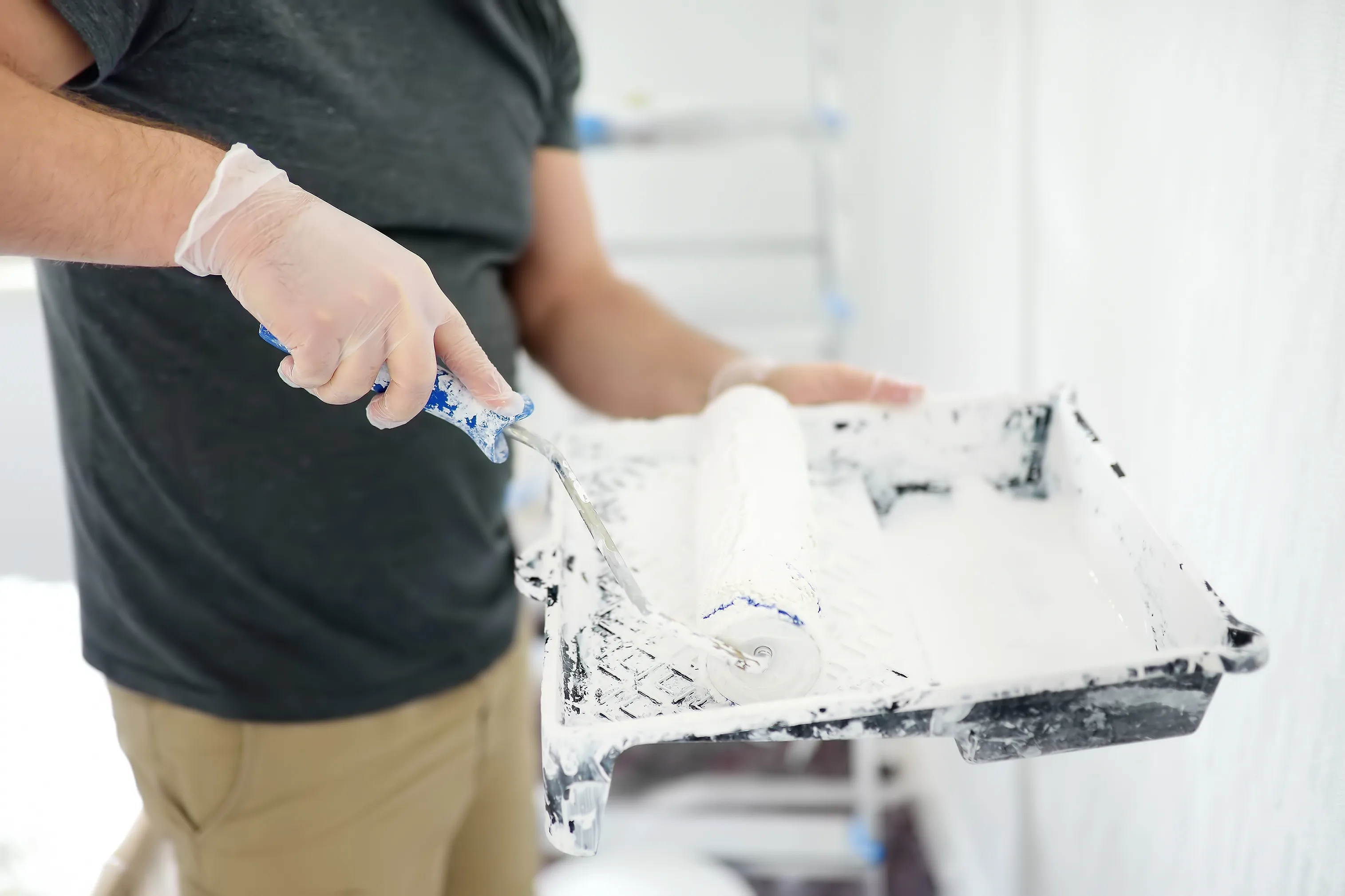 A person painting a wall with a roller while using a paint tray