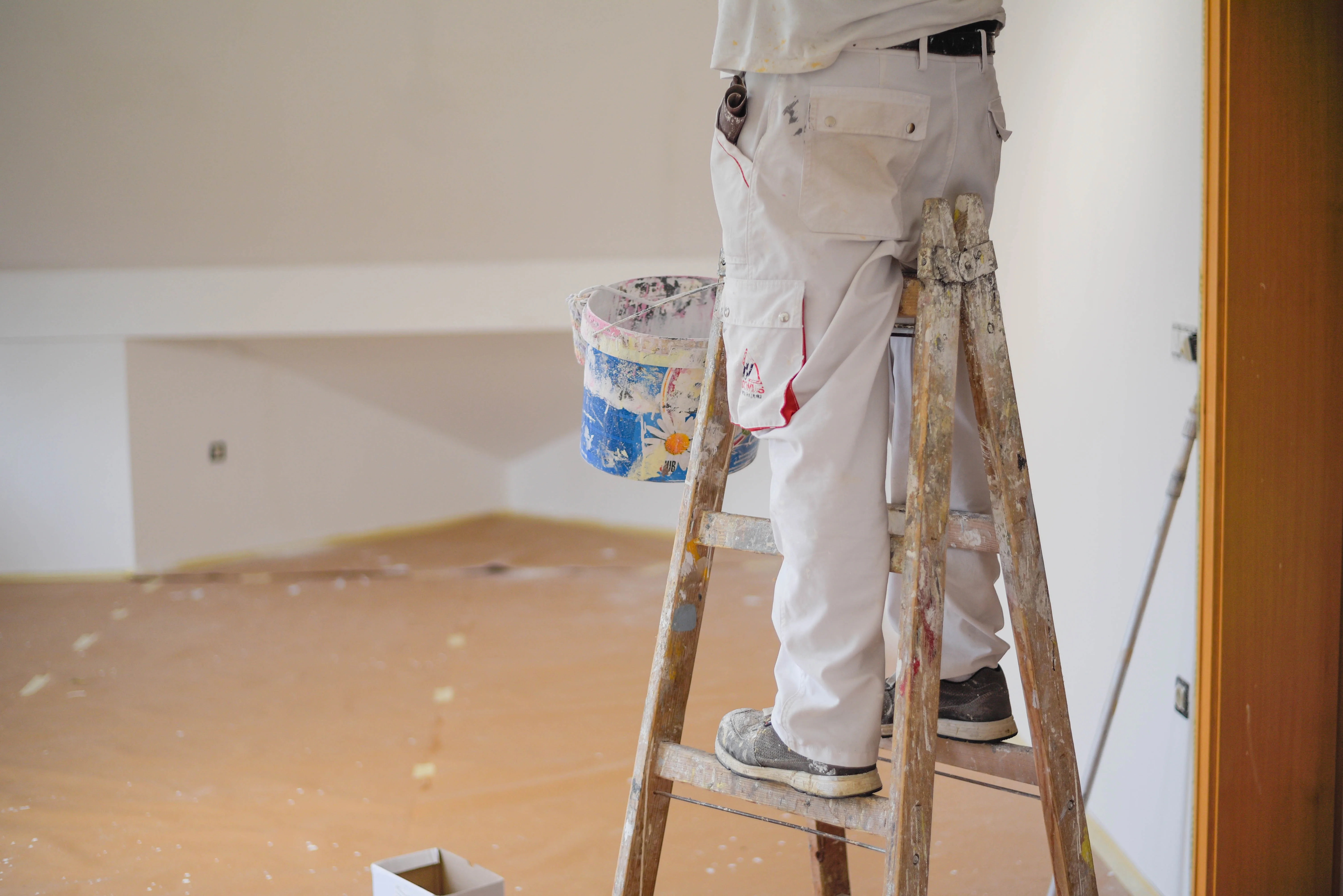 A painter standing on a ladder, preparing to paint the interior of a room with a bucket of paint