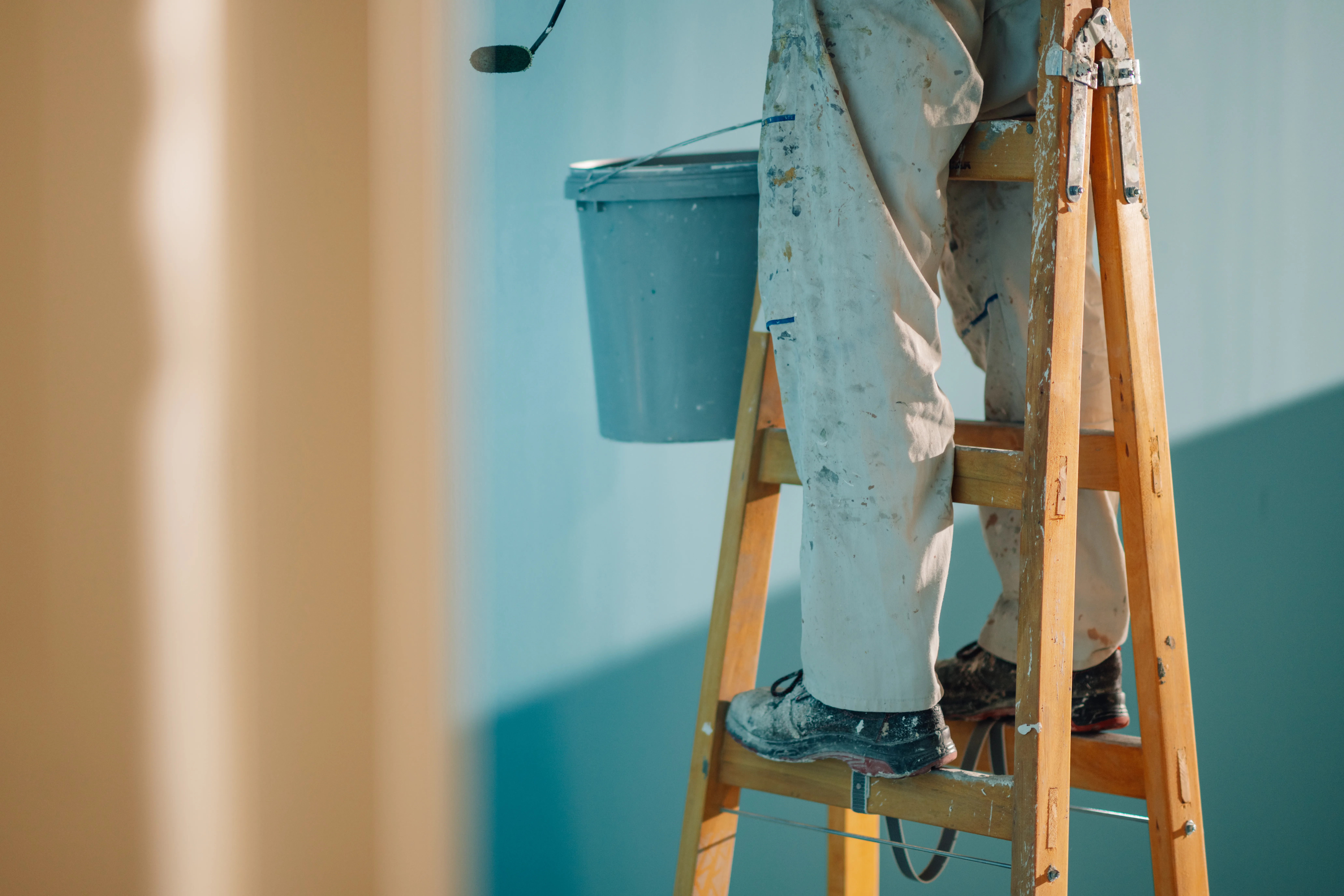A painter on a ladder applying interior wall paint with attention to detail