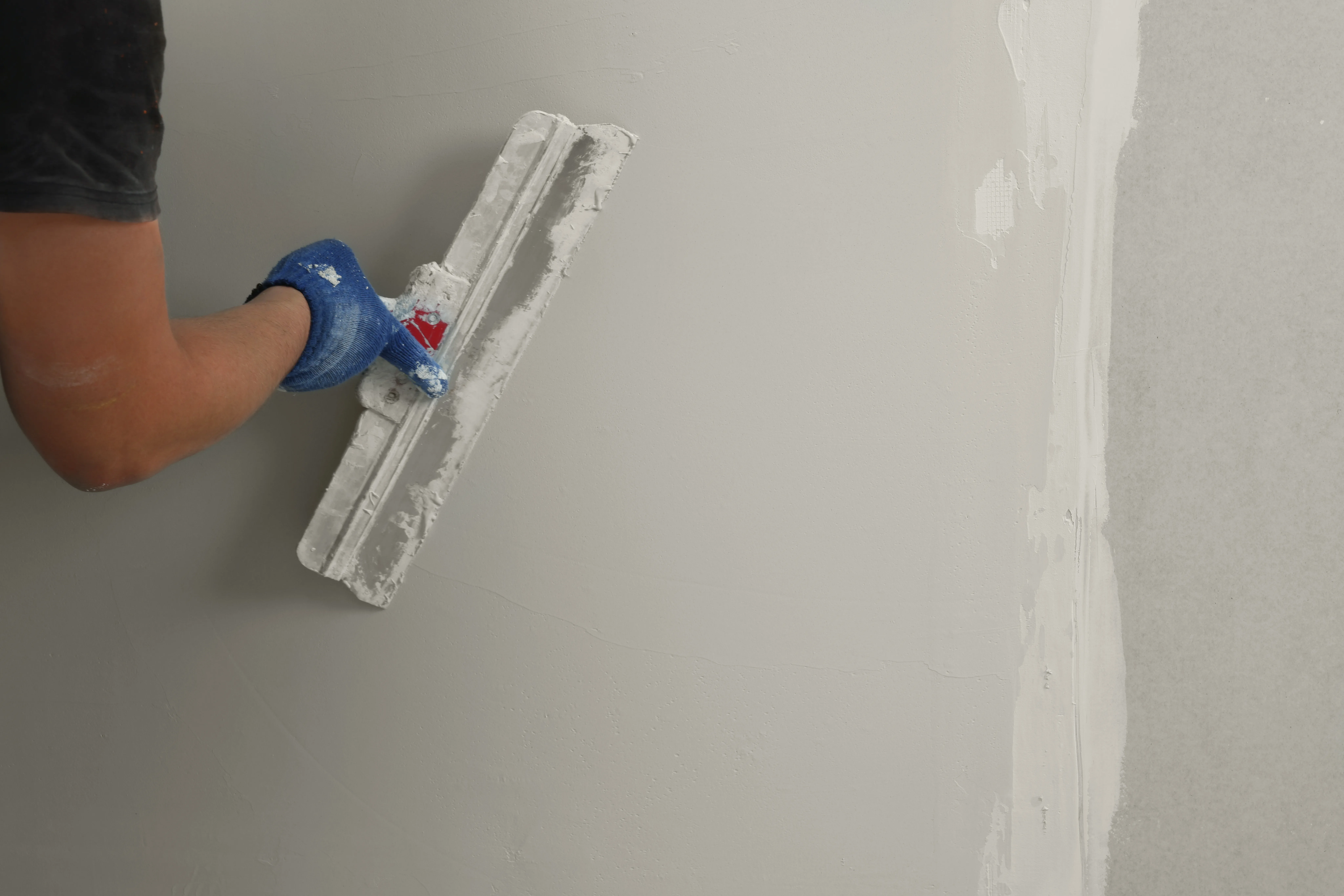 A person applying skim coat to a wall with a trowel for surface preparation