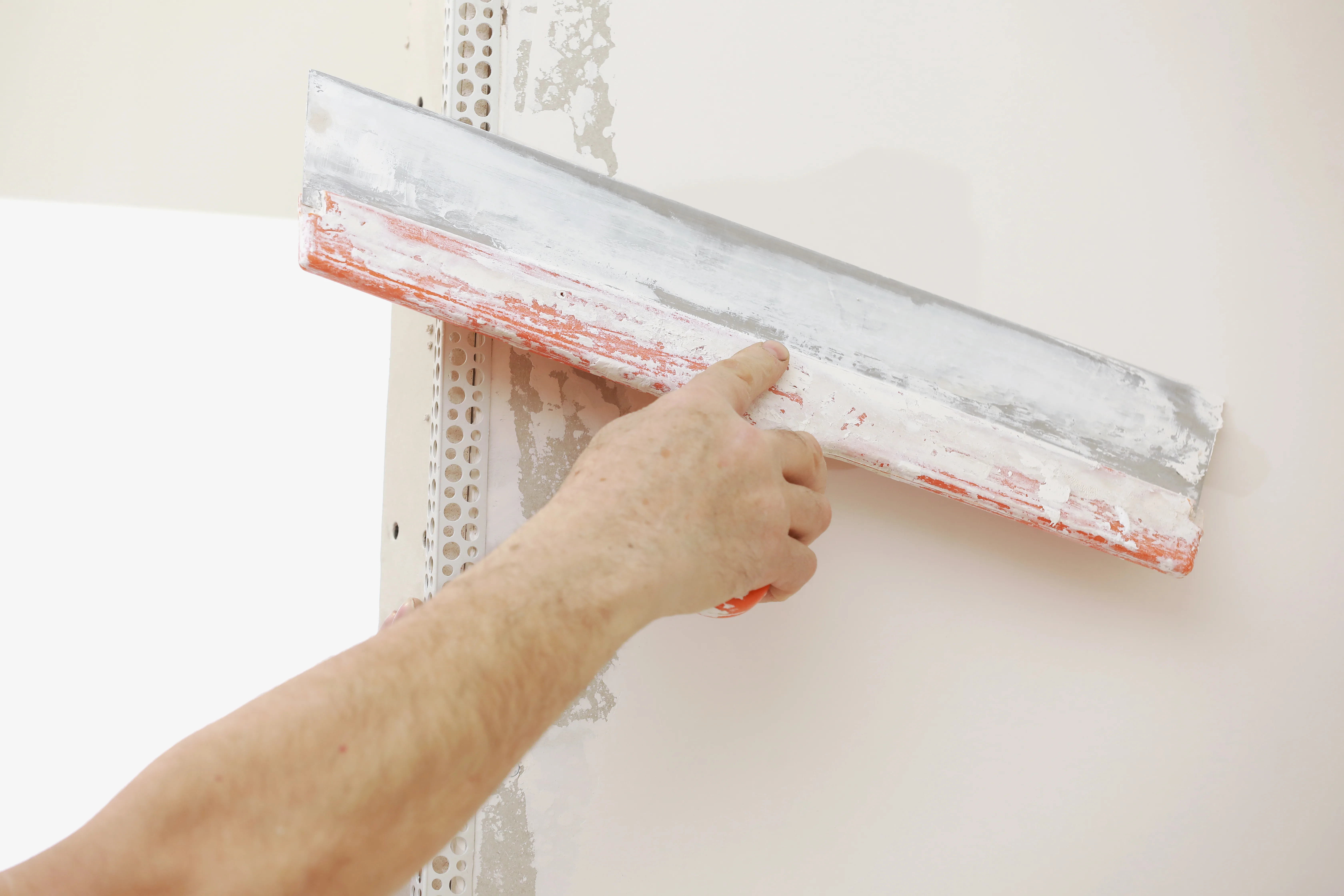 A hand applying skim coat to a wall with a smoothing trowel during surface preparation
