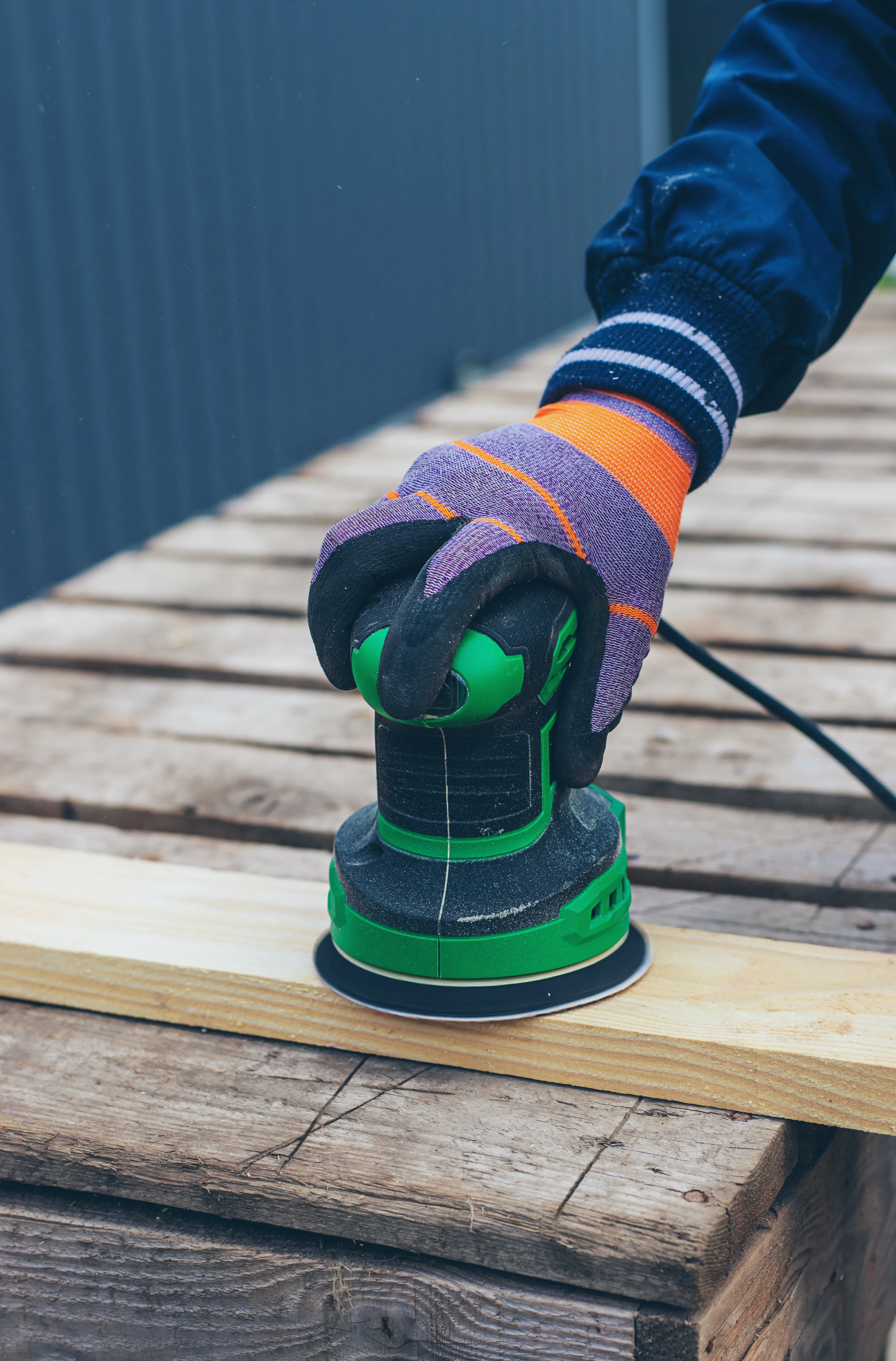 A worker sanding wood with an electric sander on a workbench