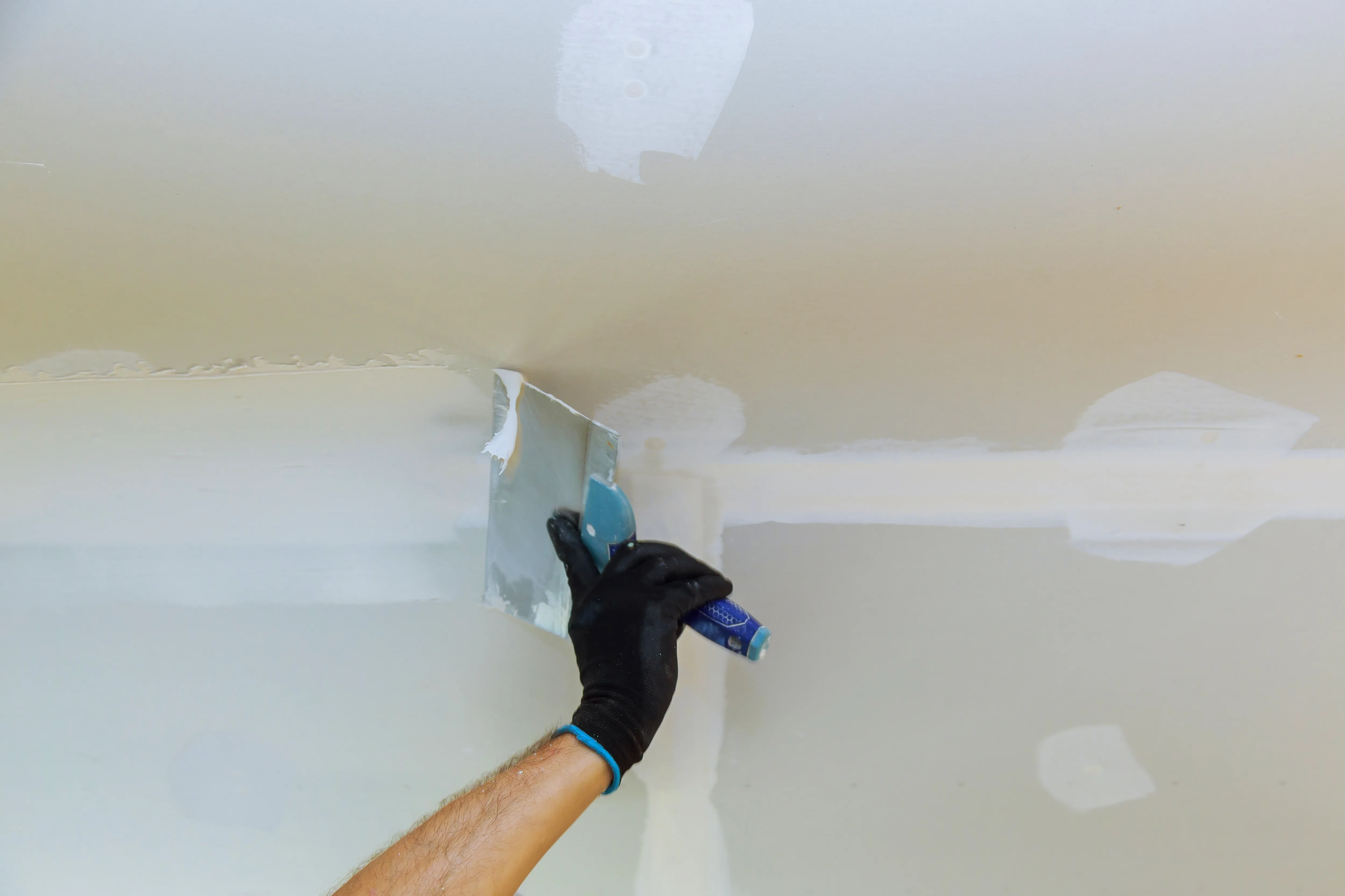 A person applying paint to a ceiling with a putty knife, showing precise interior painting work