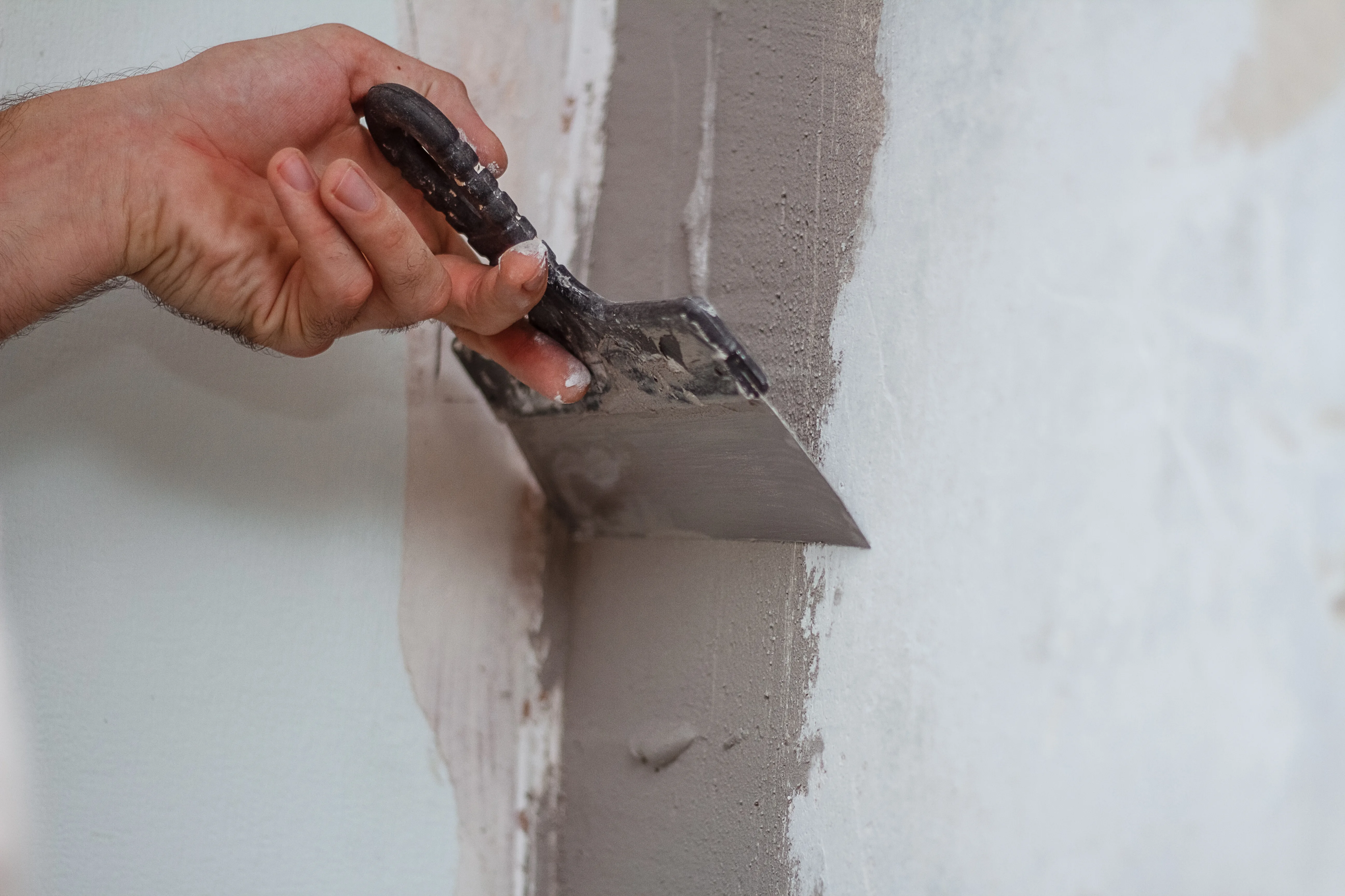 A hand using a trowel to apply plaster on a wall during surface preparation
