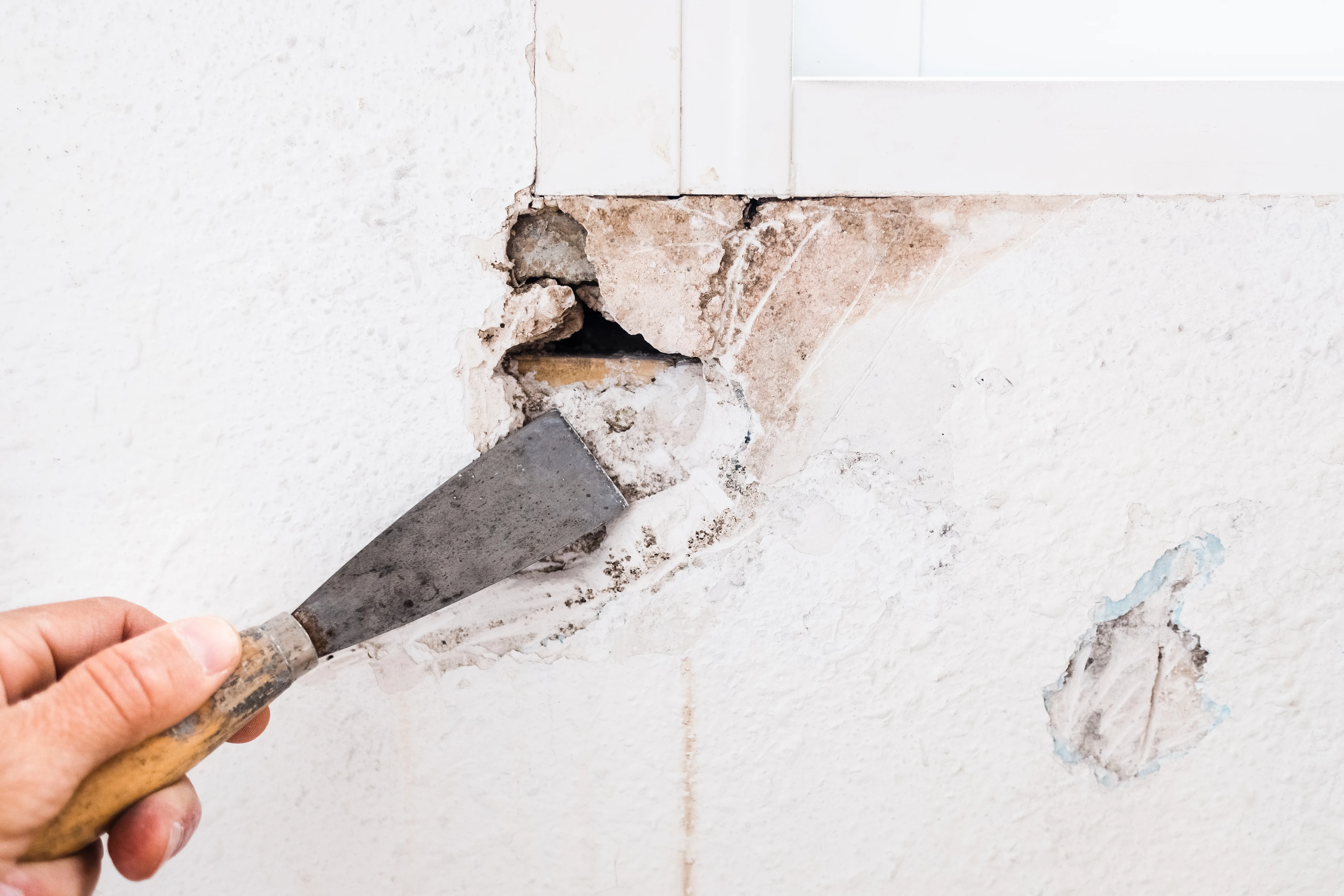 Close-up of a hand using a chisel to repair a cracked wall surface