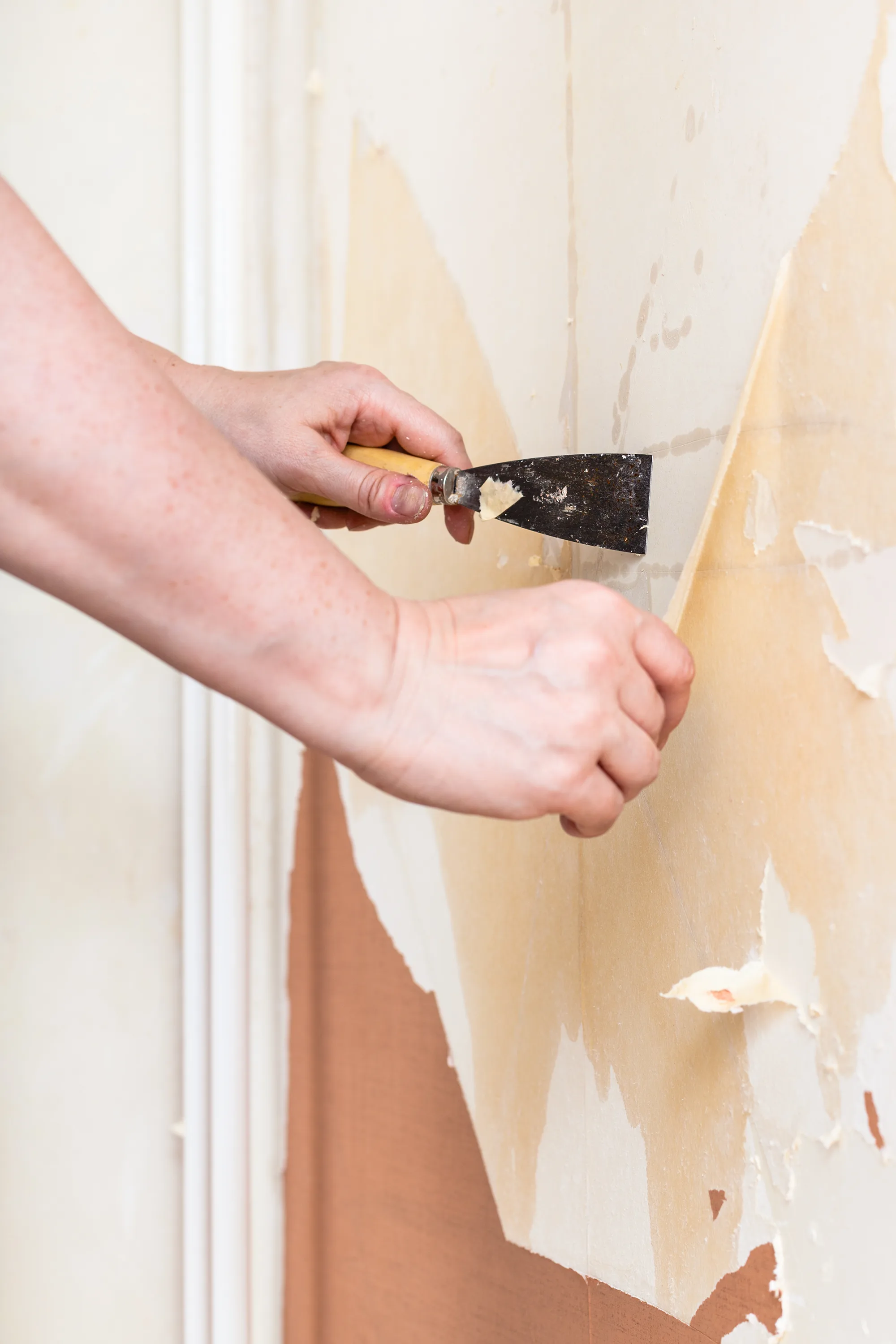 Close-up of a hand using a scraper to remove wallpaper from a wall during a renovation project
