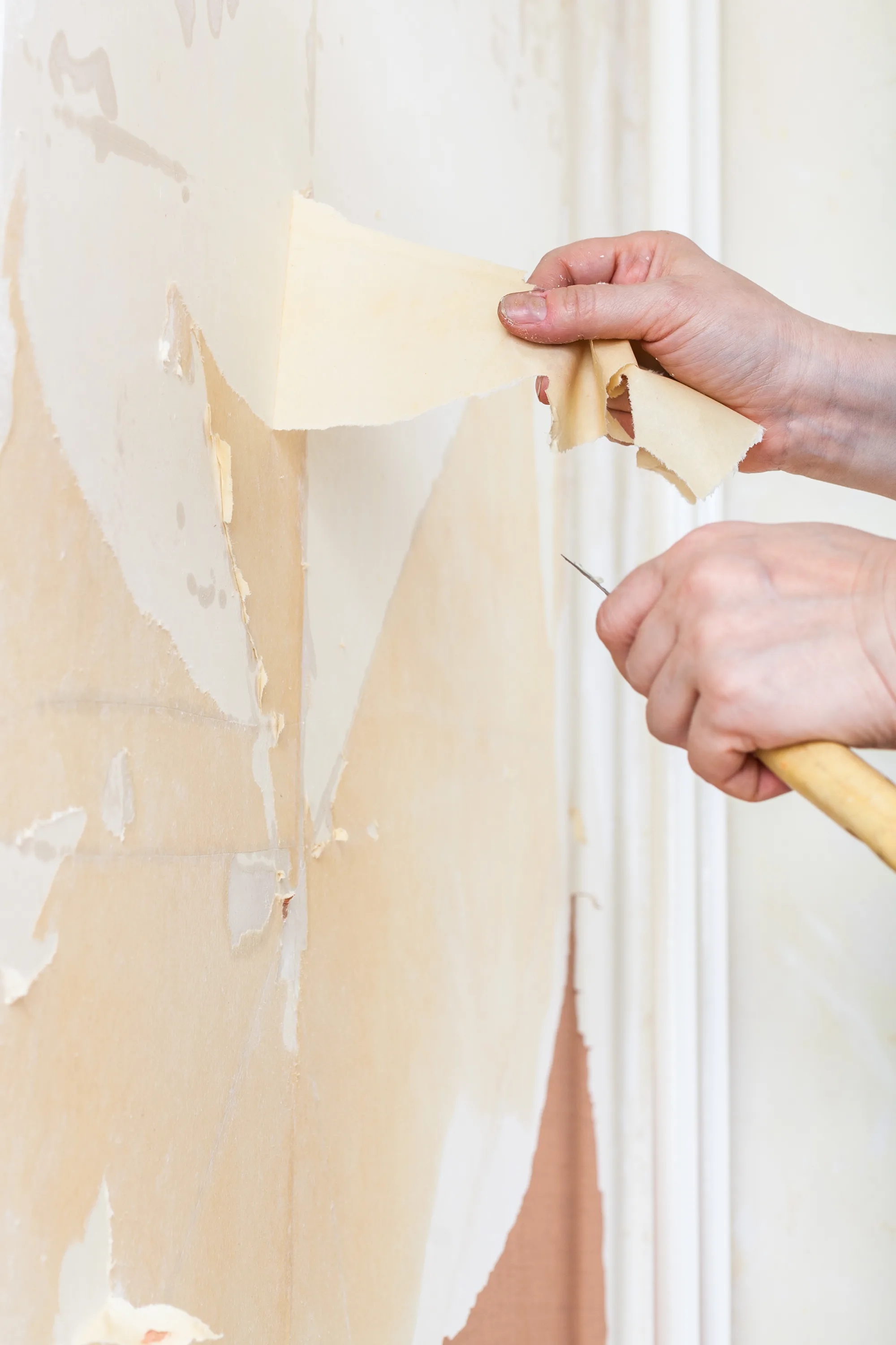 A close-up of hands removing wallpaper from a wall, preparing it for decoration