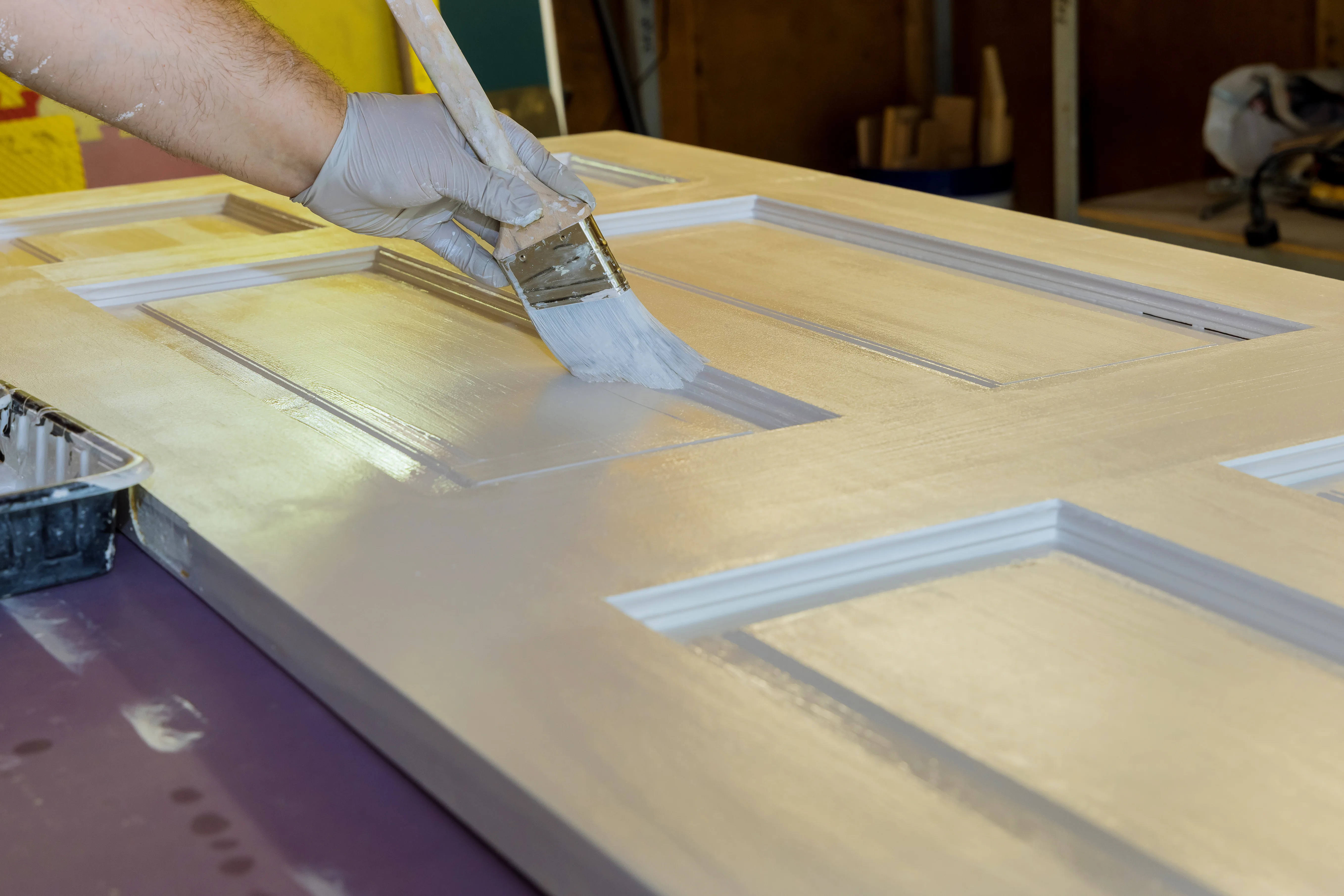 A person painting a wooden door with a brush in a workshop setting