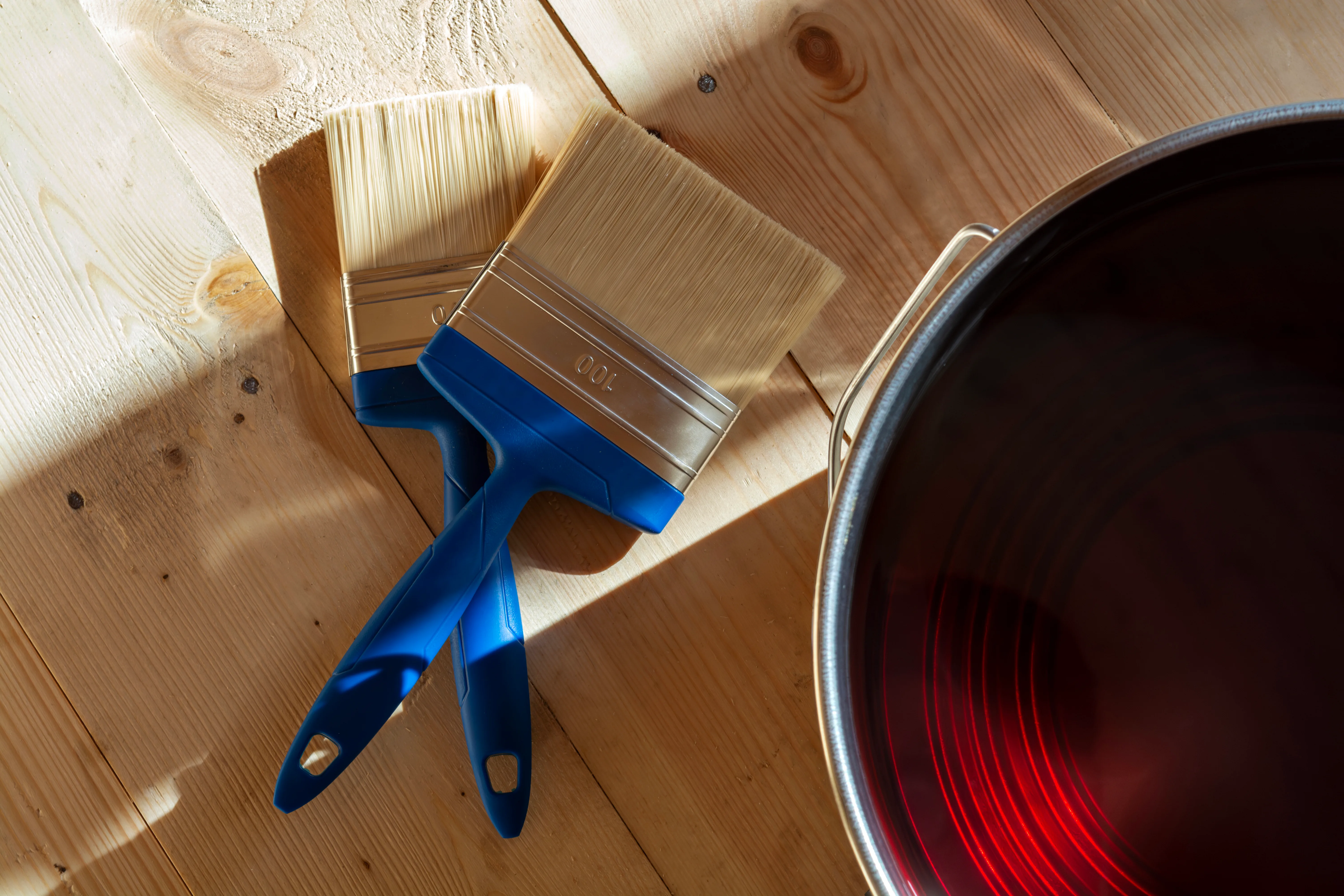 Two paintbrushes and a can of red paint on a wooden surface