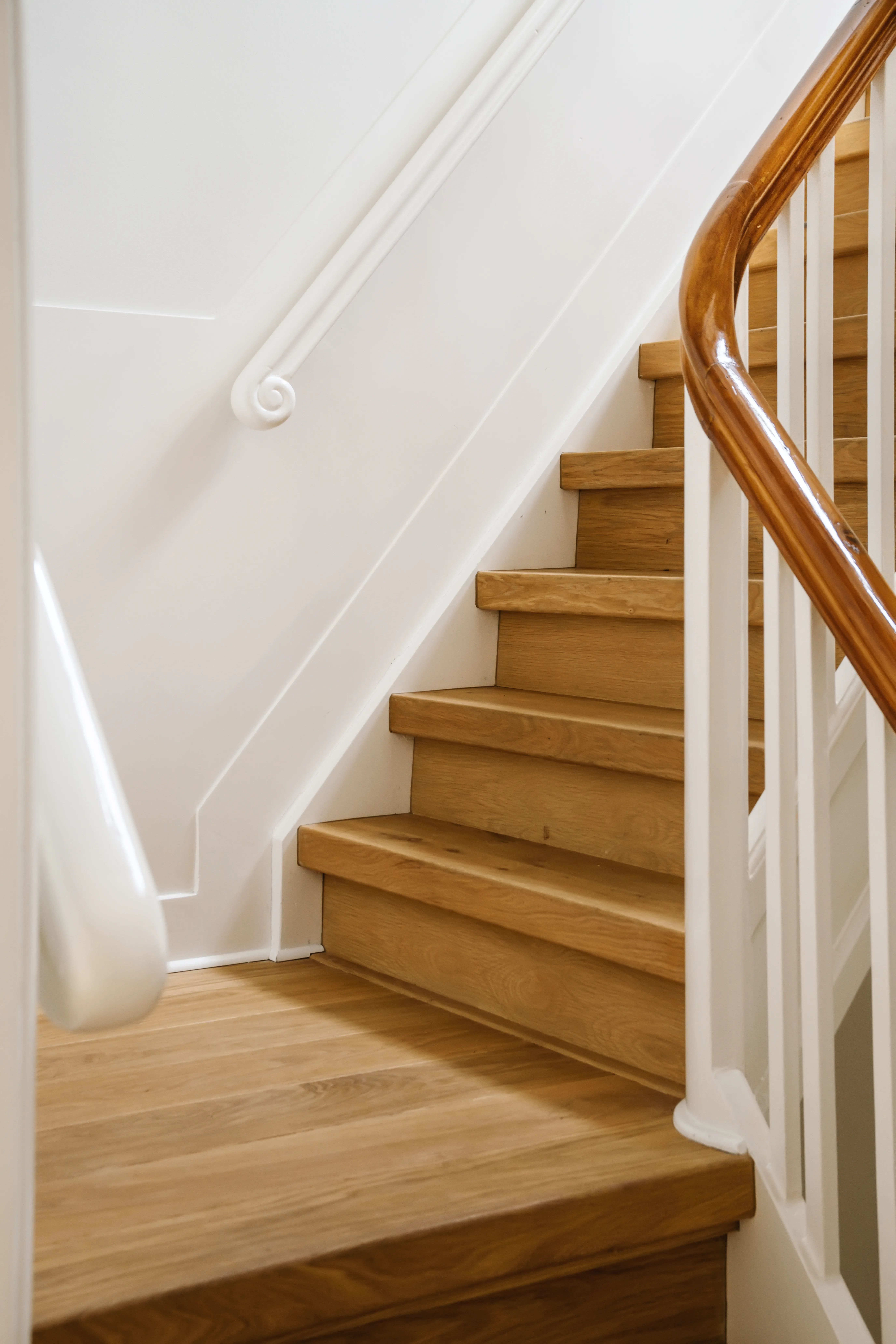 A well-lit interior staircase featuring wooden steps and a white railing, showcasing high-quality craftsmanship